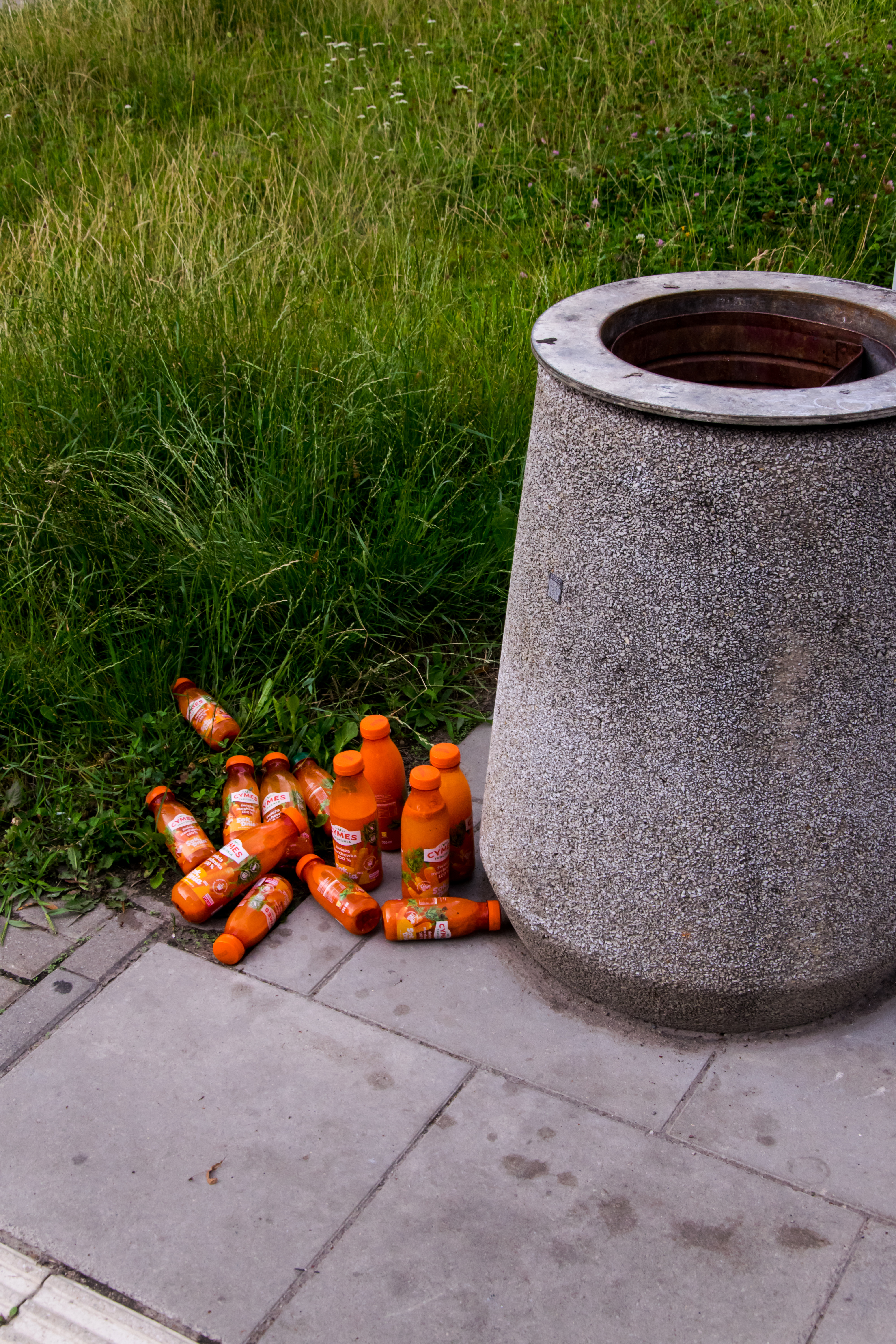 a dozen of carrot juice bottles next to trash bin