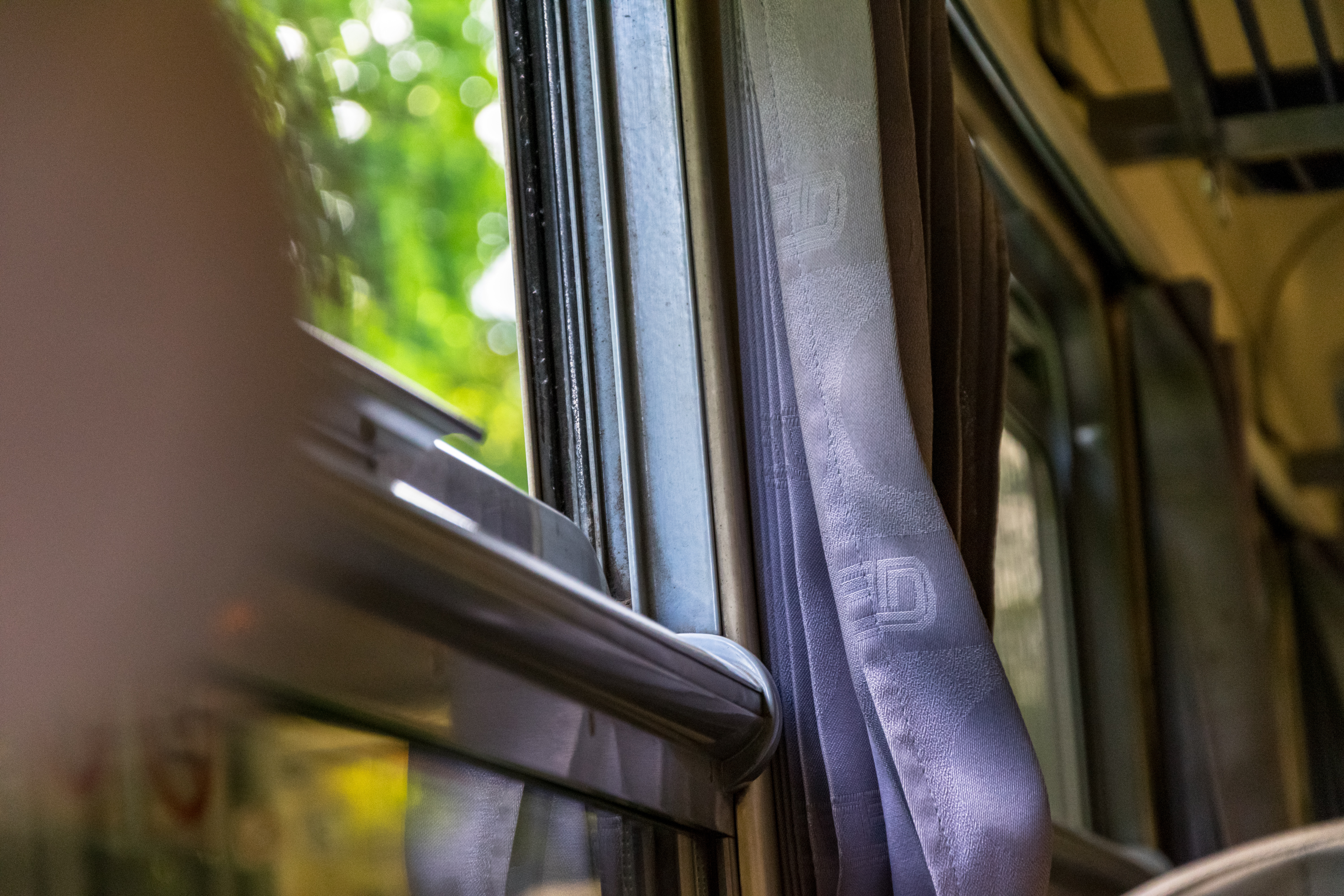 train interior, photo is focused on a grey patterned curtain next to opened window, outside is heavily blurred 