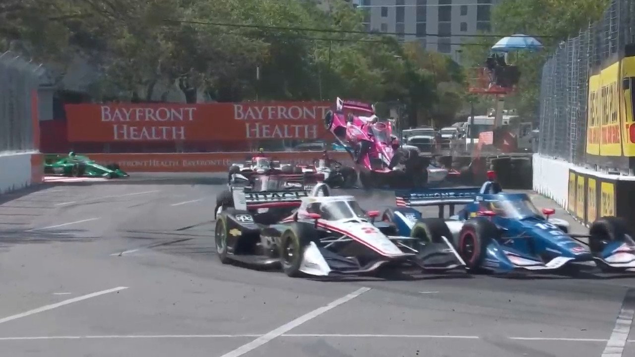 the pink car of kyle kirkwood is in the air, basically above 2 other cars, almost facing towards us