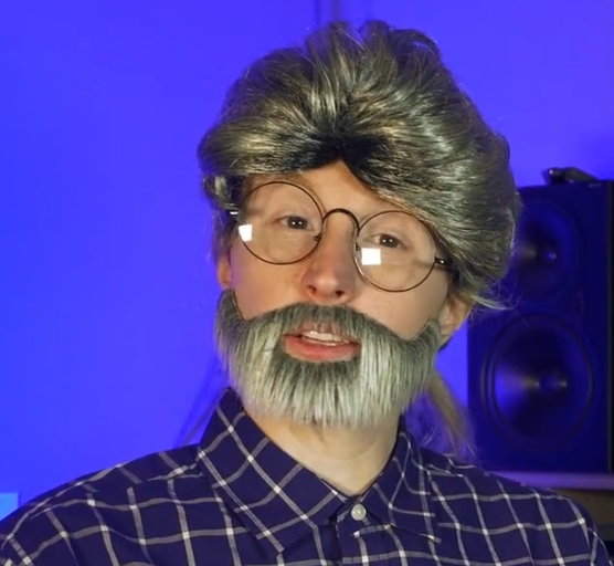 jessie gender cosplaying as george lucas, with a wig, fake beard and a blue shirt