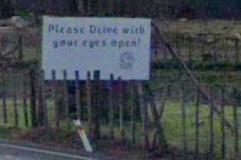 low pixel count screenshot of google street view sign that says "Please Drive with your eyes open"