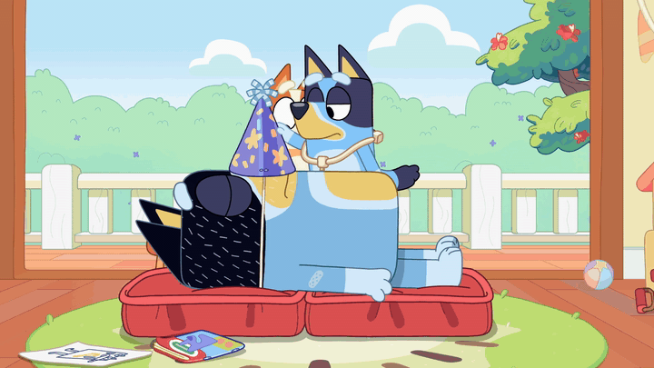 bandit has a party hat with it's strings wrapped around his head. the hat itself is on his nose. bluey pulls it up, says "wake up mate" (not captioned), then releases it, hitting bandit in the face.