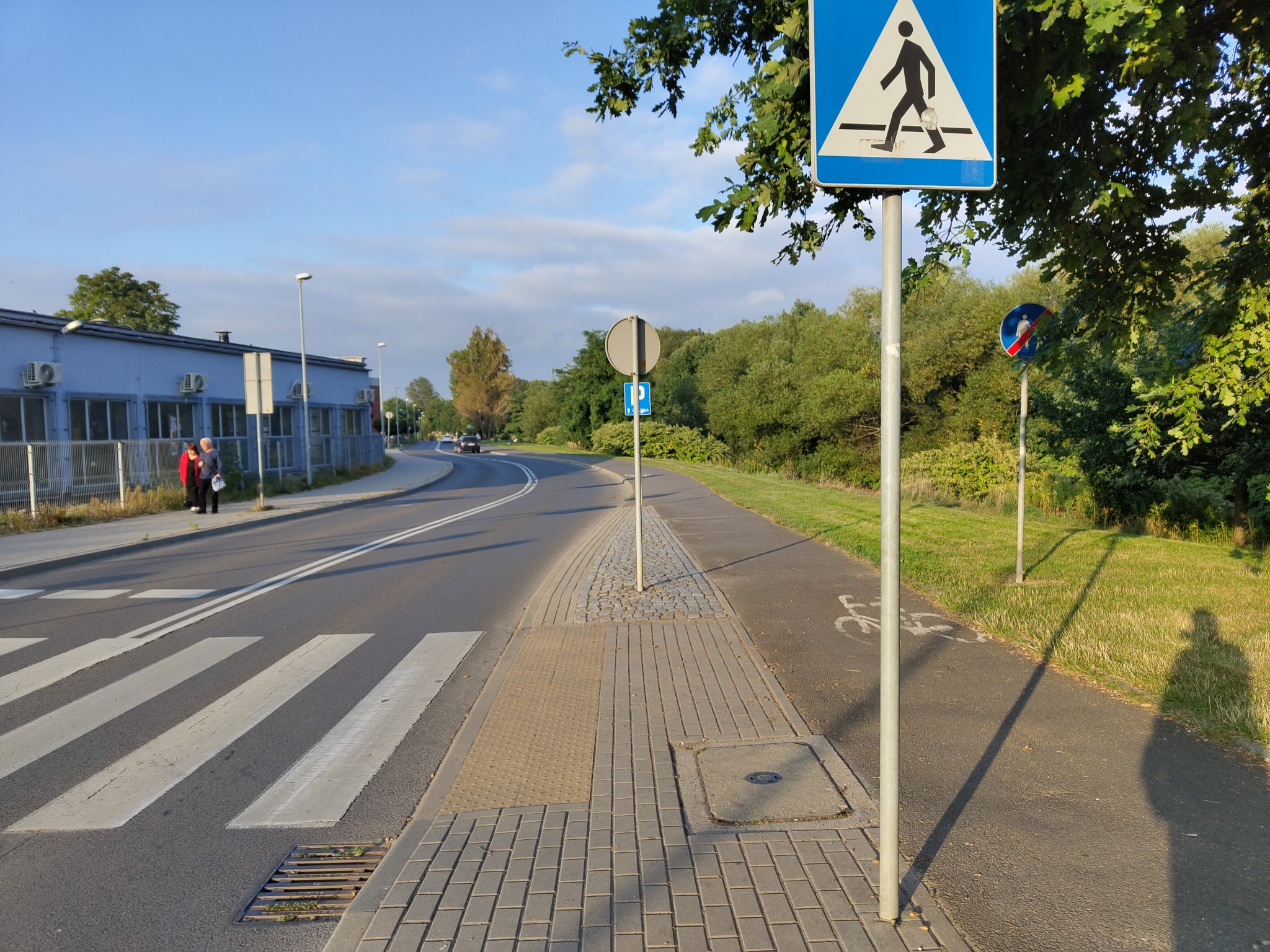 photo of a sidewalk abruptly ending, and bike path continuing, with pedestrians having to cross the street in order to continue, there's a lot of space for a sidewalk between bike path and benches on the right