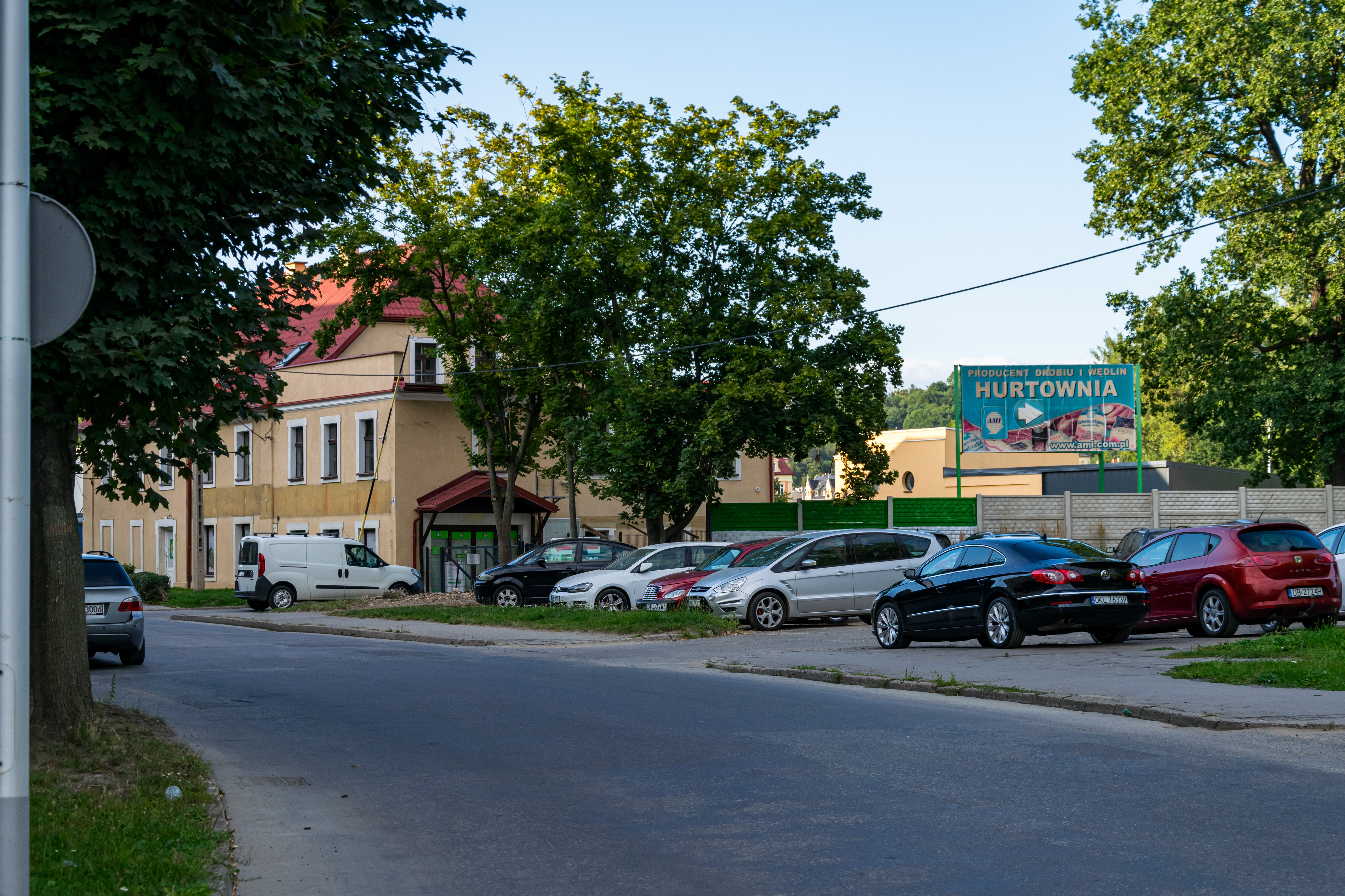 a street with a bunch of cars parked, a building and a sign saying "hurtownia"
