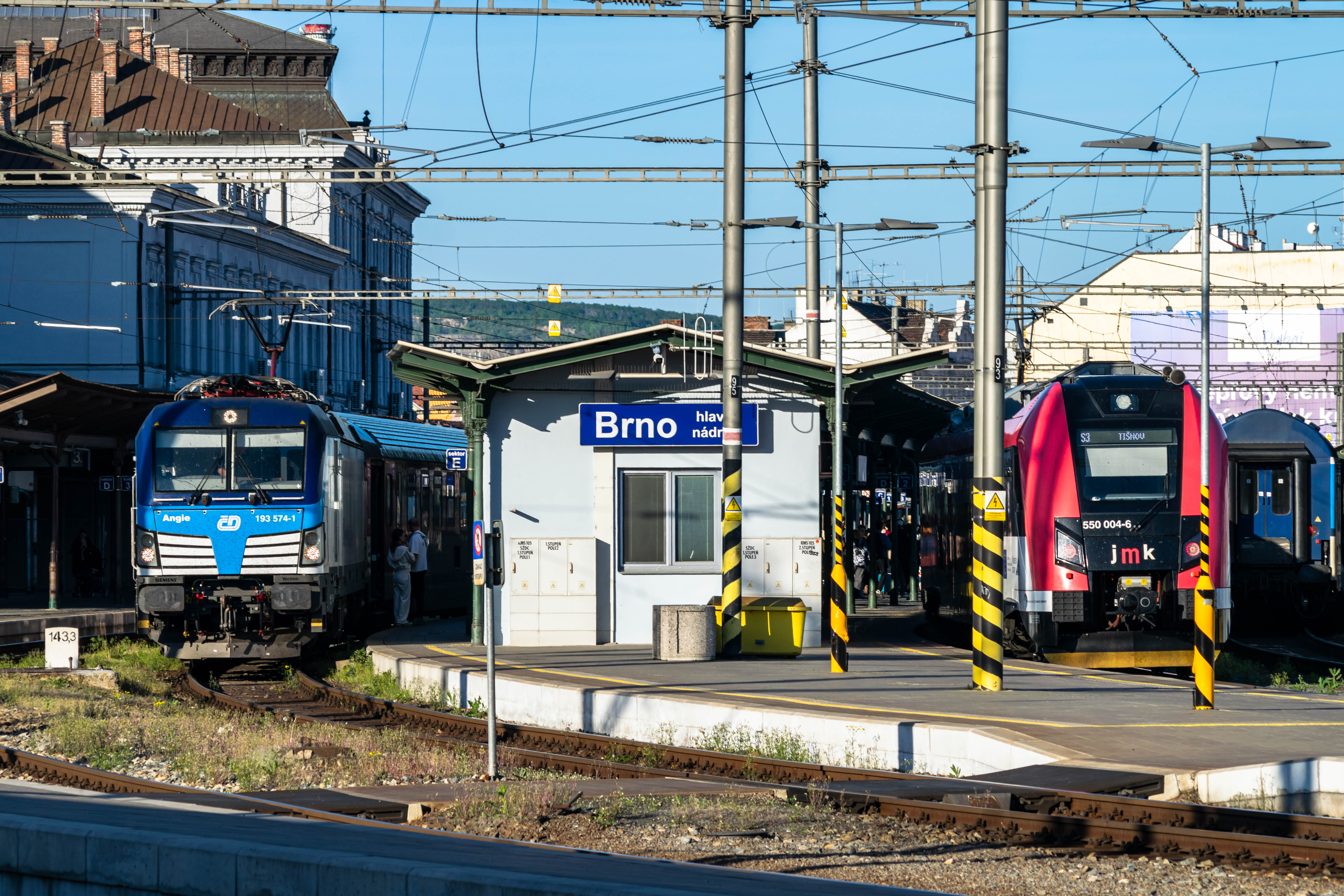 blue-white locomotive standing next to a white-red-black EMU