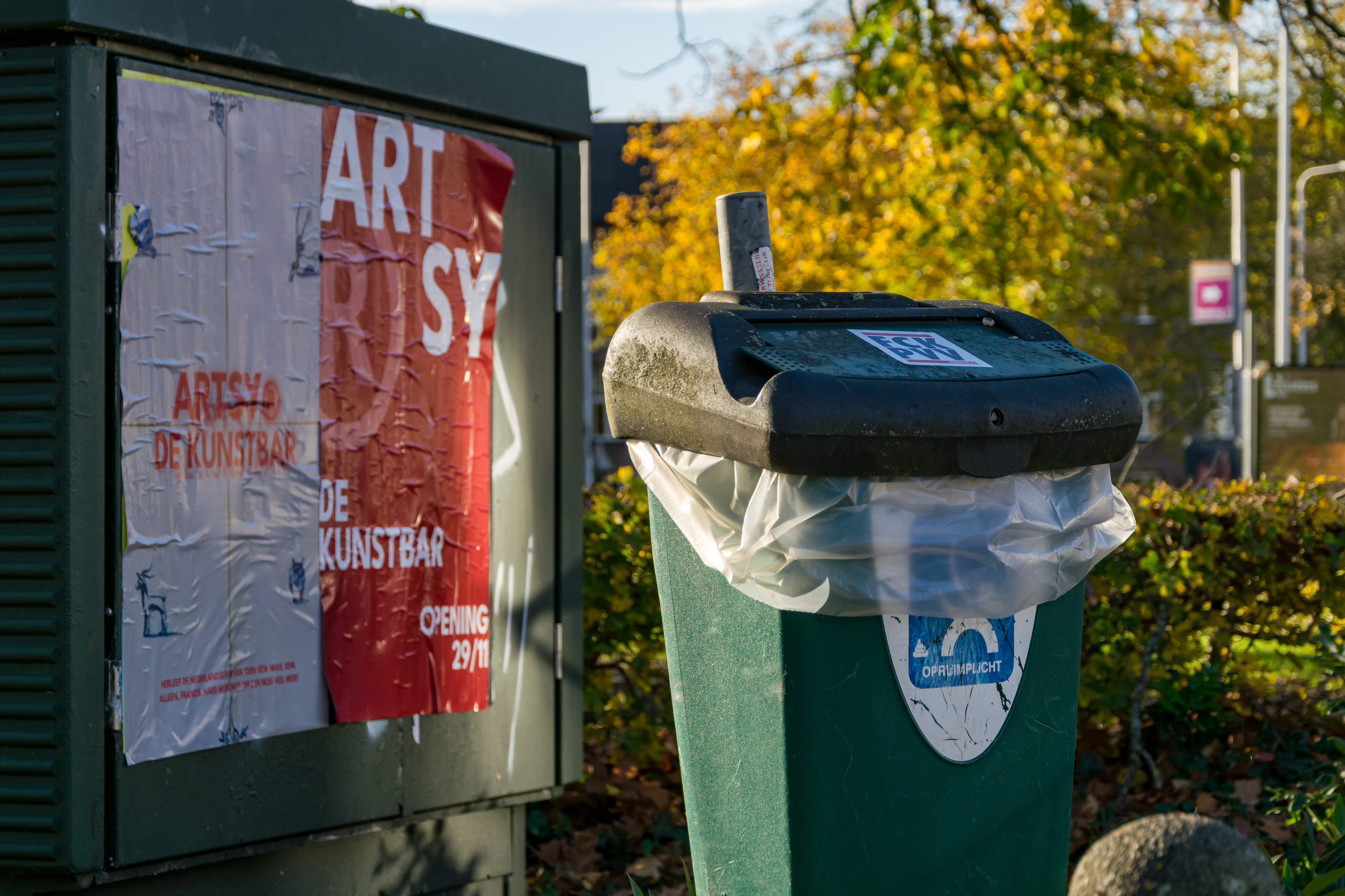 Trash can with a fuck pvv sticker on a cover, next to some bulletin board