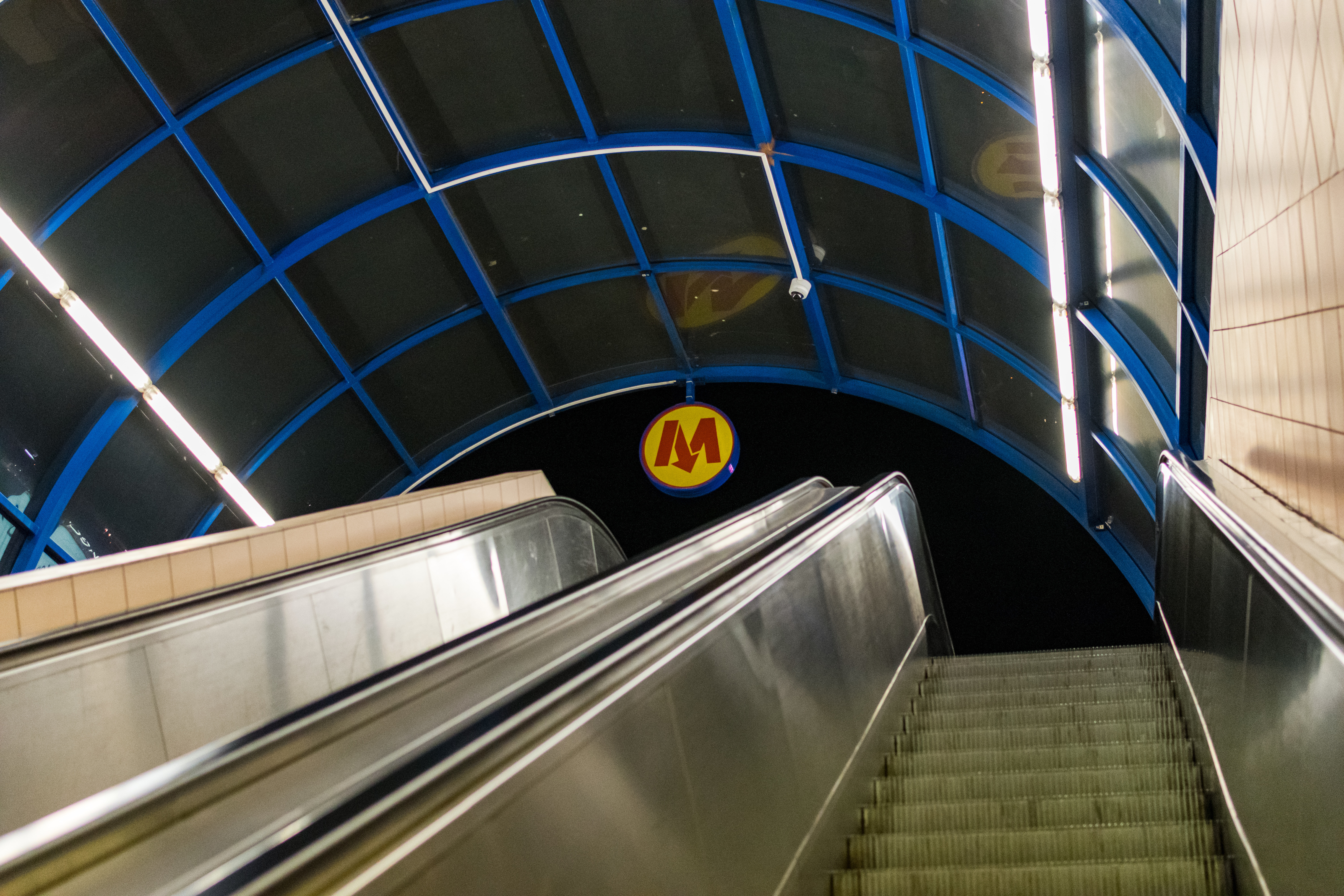 Escalator out of metro station, with metro logo in the middle