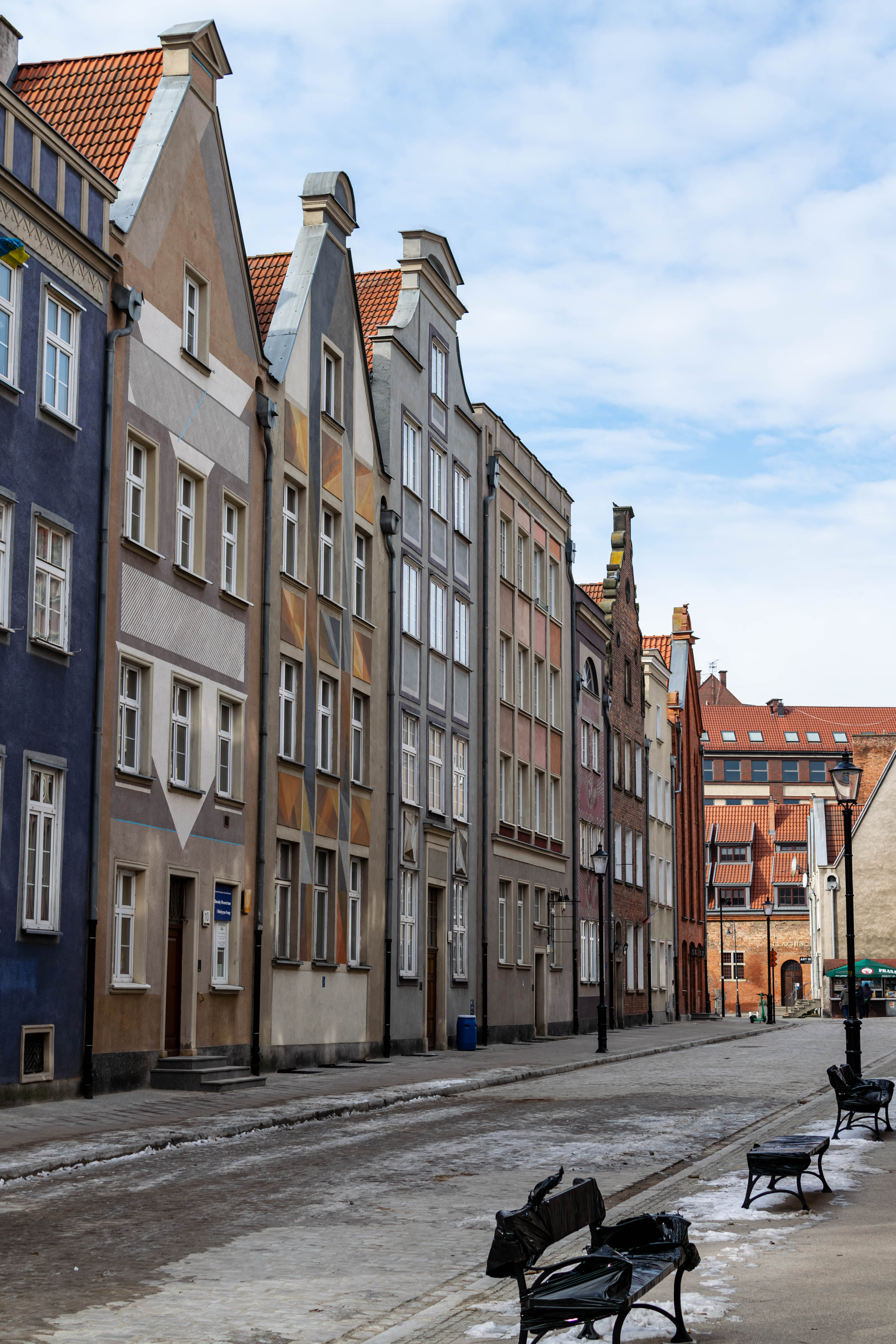 yet another street but with less colorful townhouses, there are remnants of snow on the street, and wrapped benches