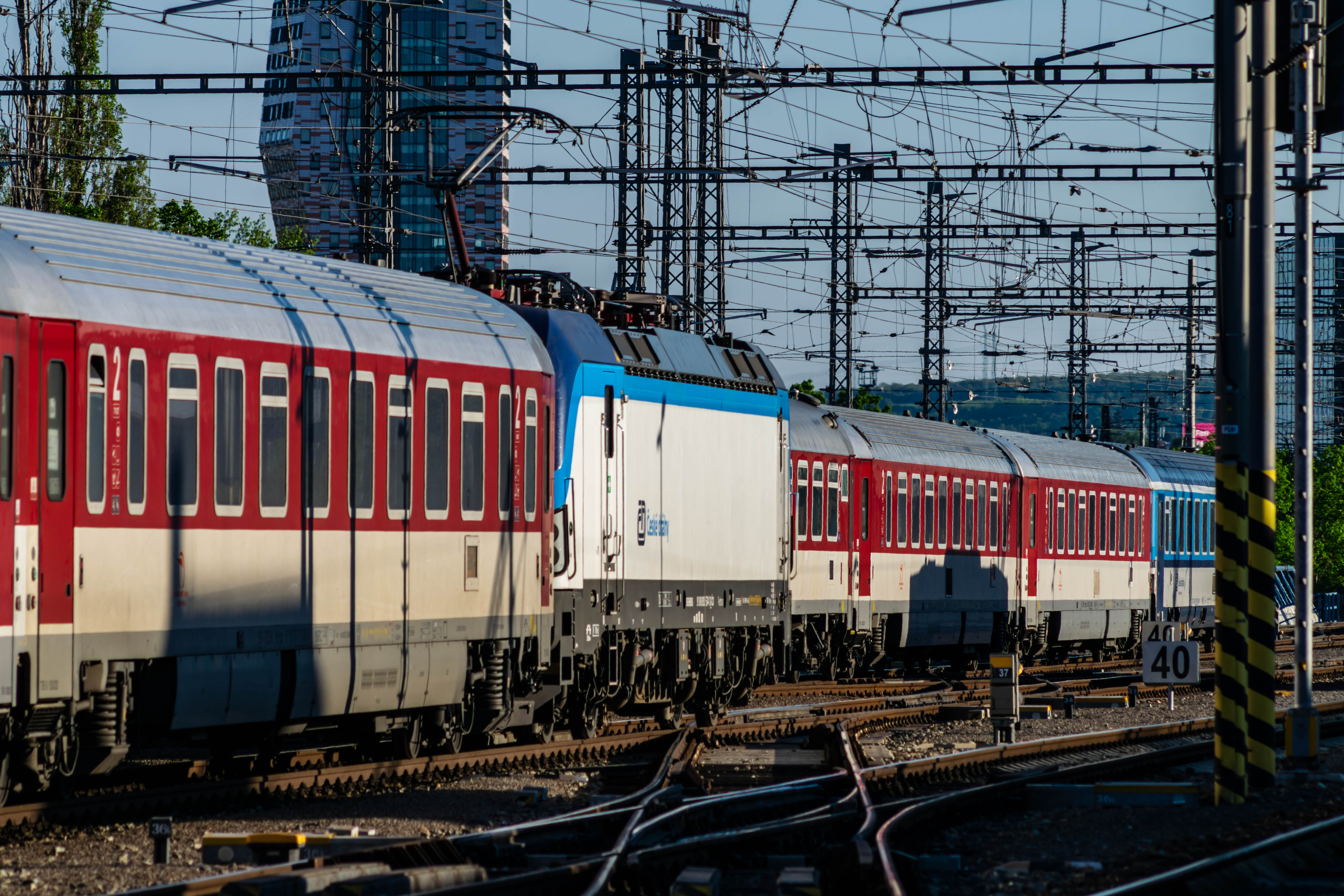 train with blue-white locomotive and red-white coaches going past another train with red-white coaches