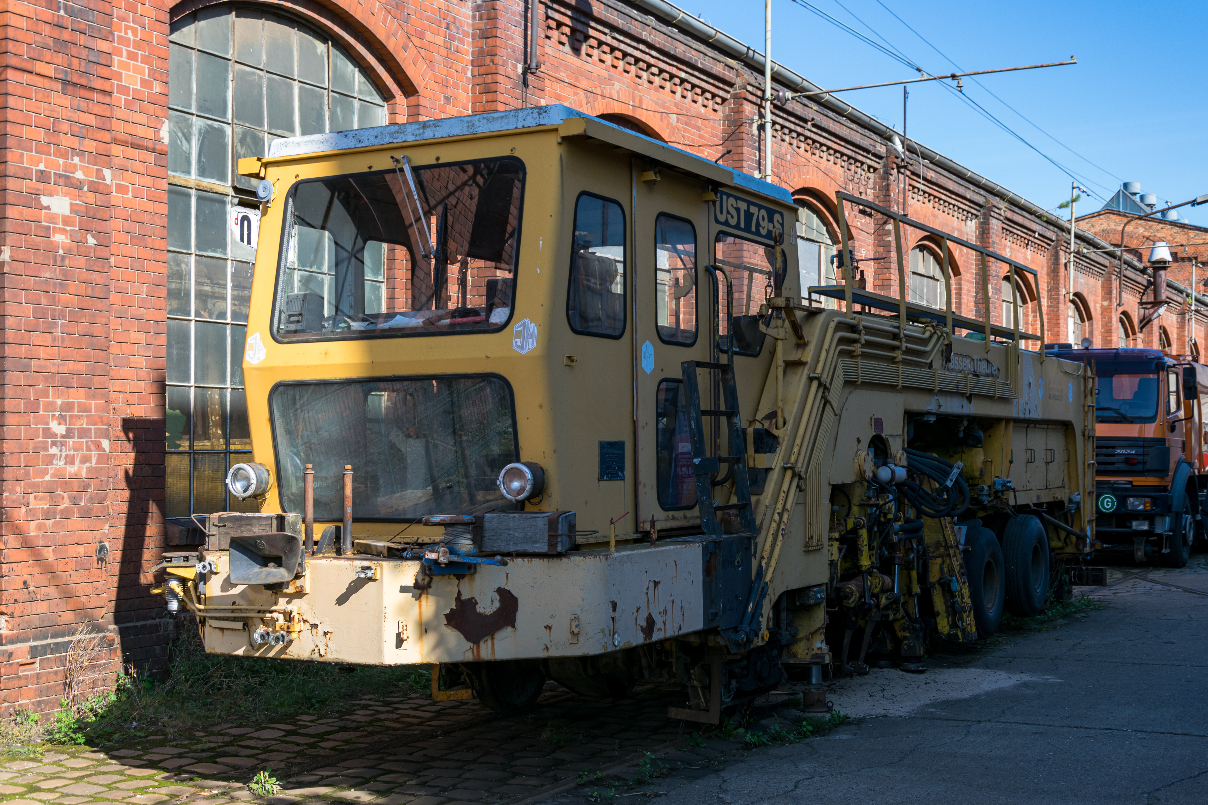 old, rusted yellow maintenance vehicle parked beside a tram depot