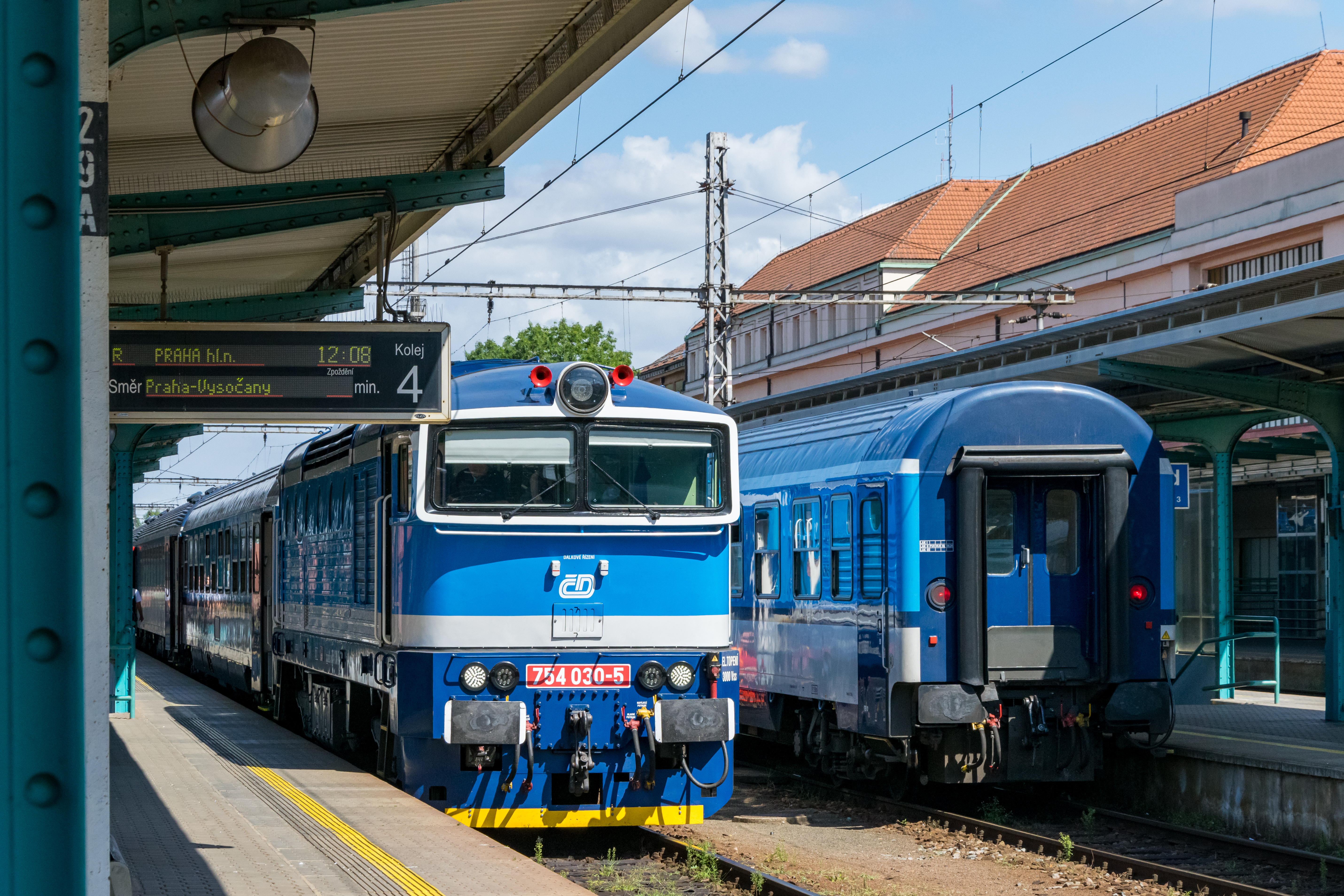 two blue-white trains standing, one of them is pulled by a diesel locomotive which is about to get disconnected
