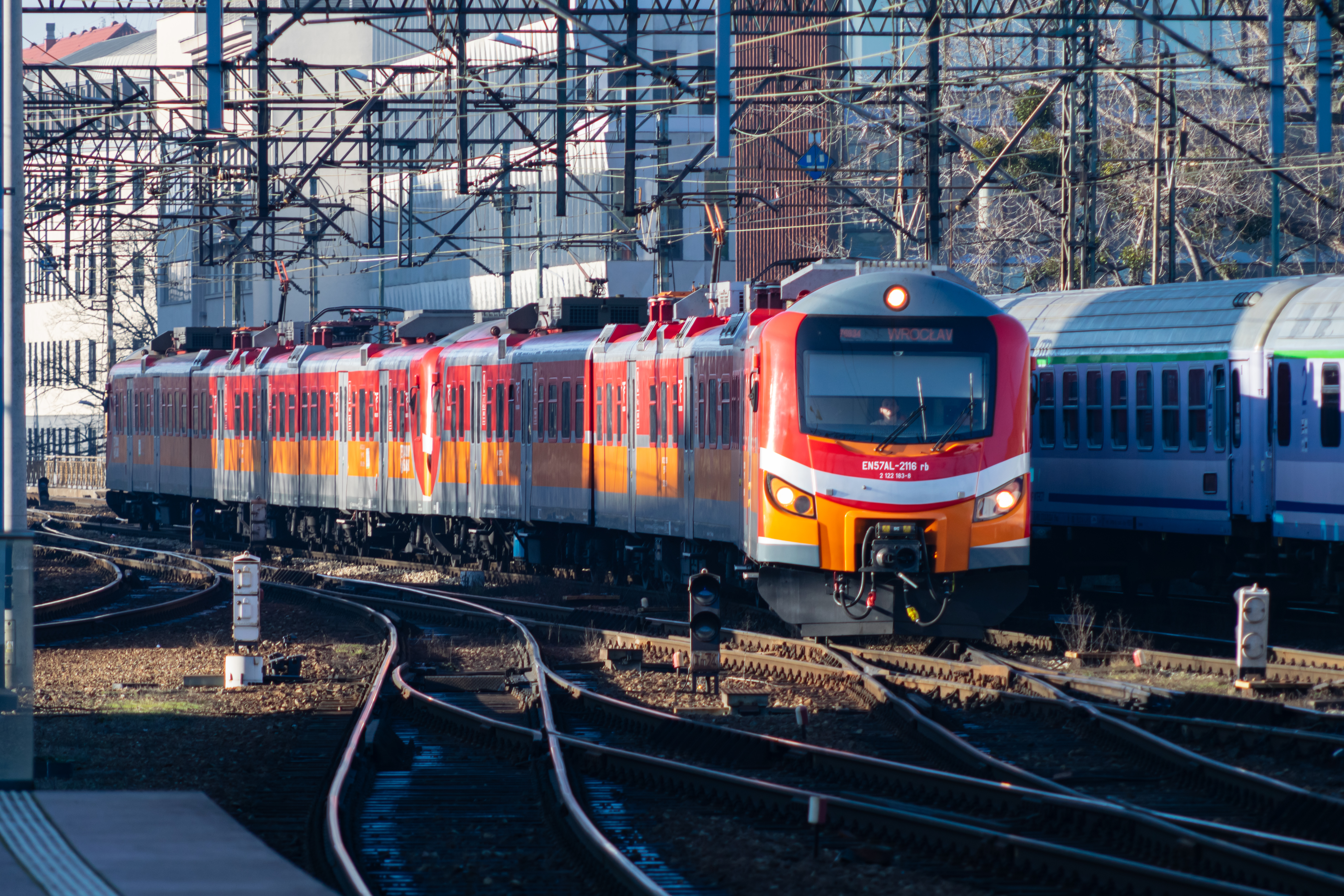 double red-orange EN57AL arriving at the station, going past a TLK train