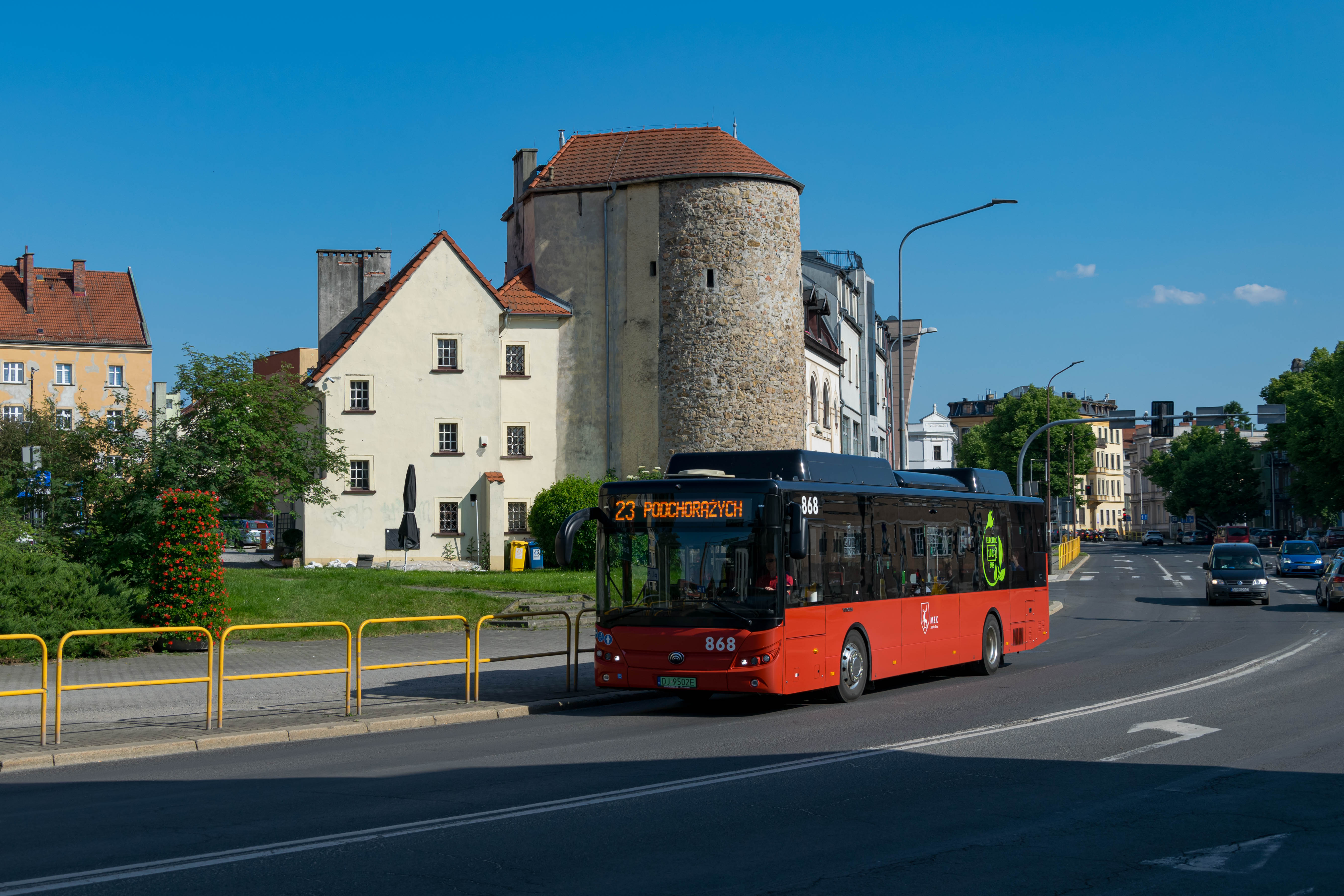 red bus on a wide street with stone building in the background