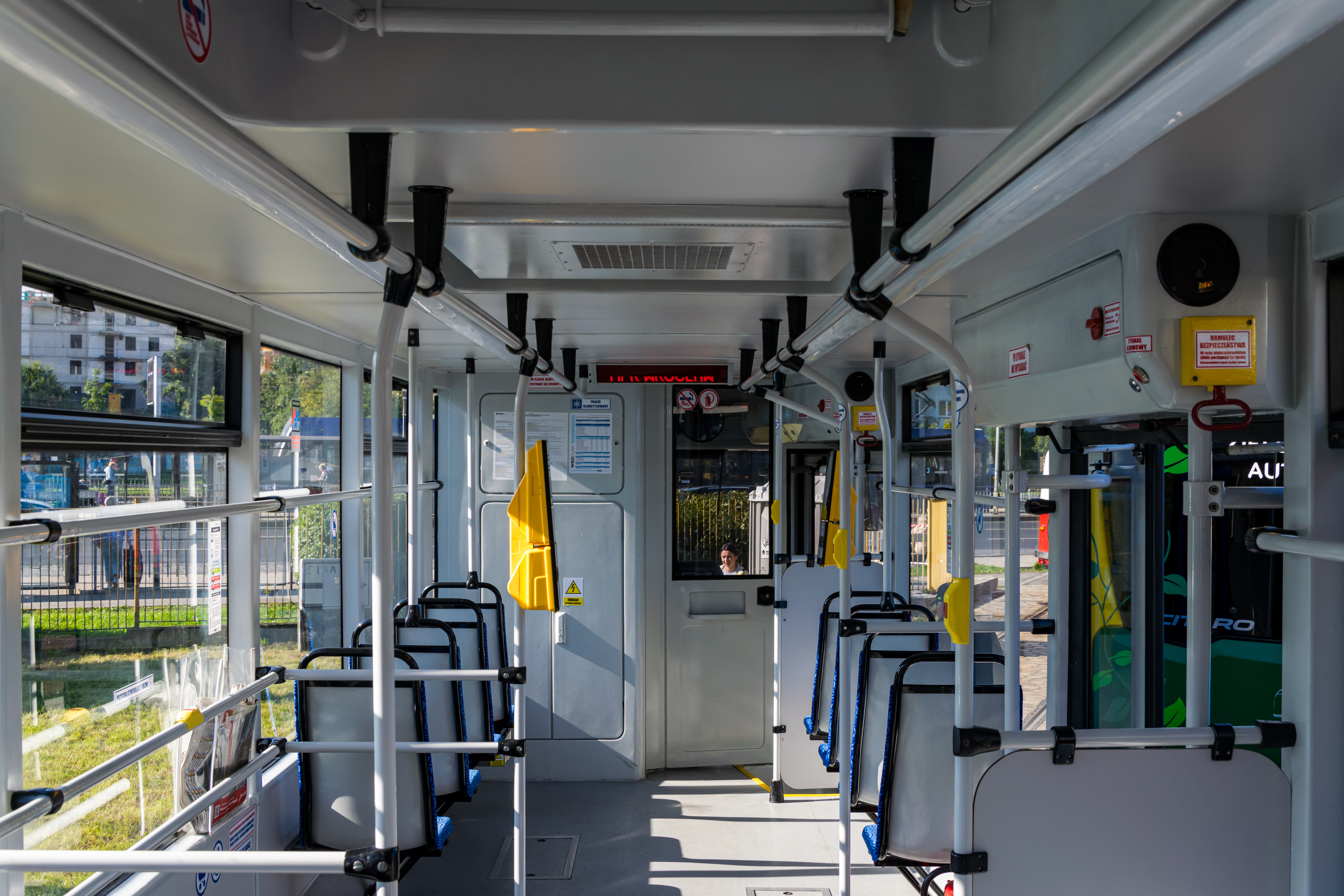 empty tram interior with white handles, back of the seats, ticket validators, and large windows visible