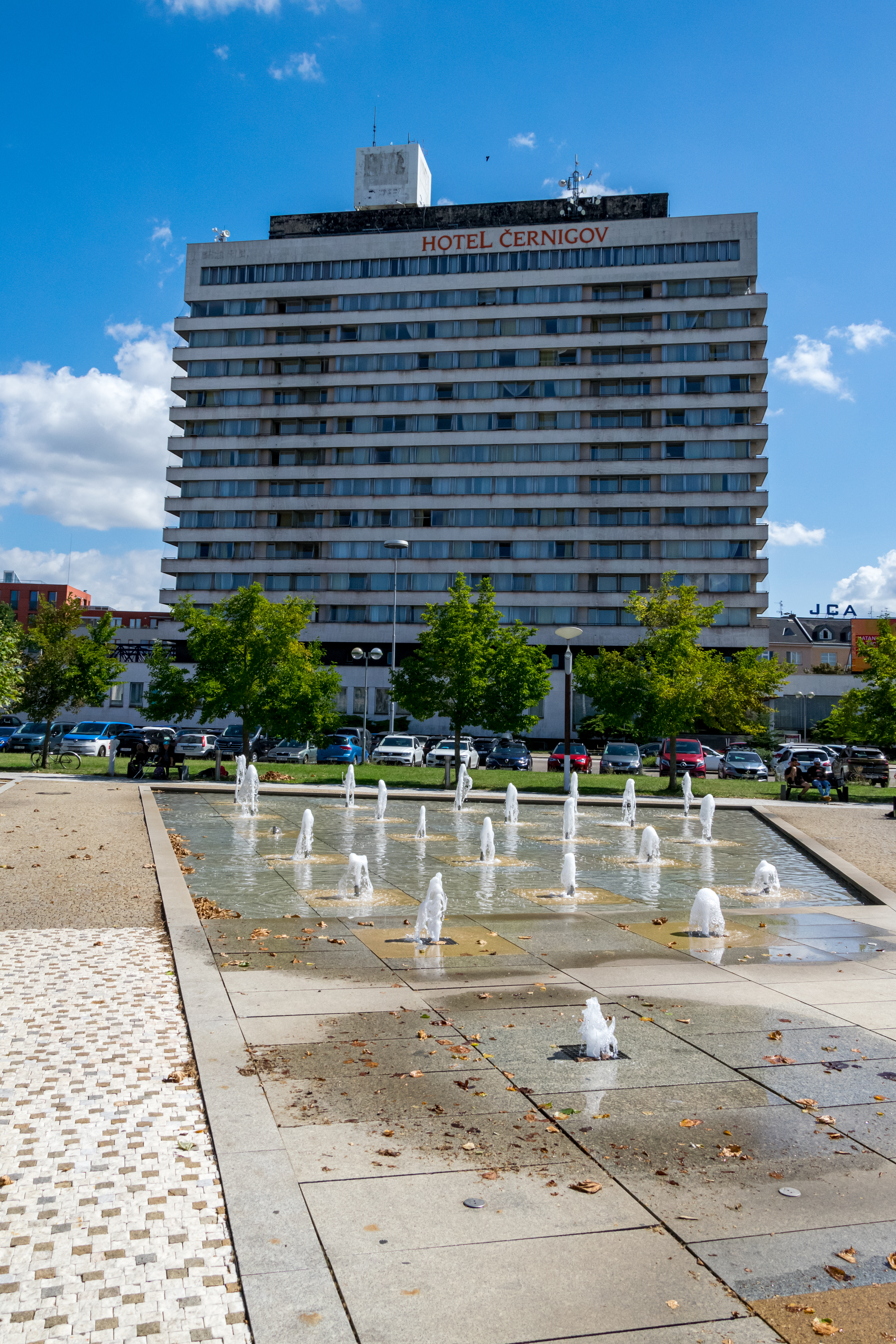 modernist hotel building dominating over a square with a small built-in fountain and some trees