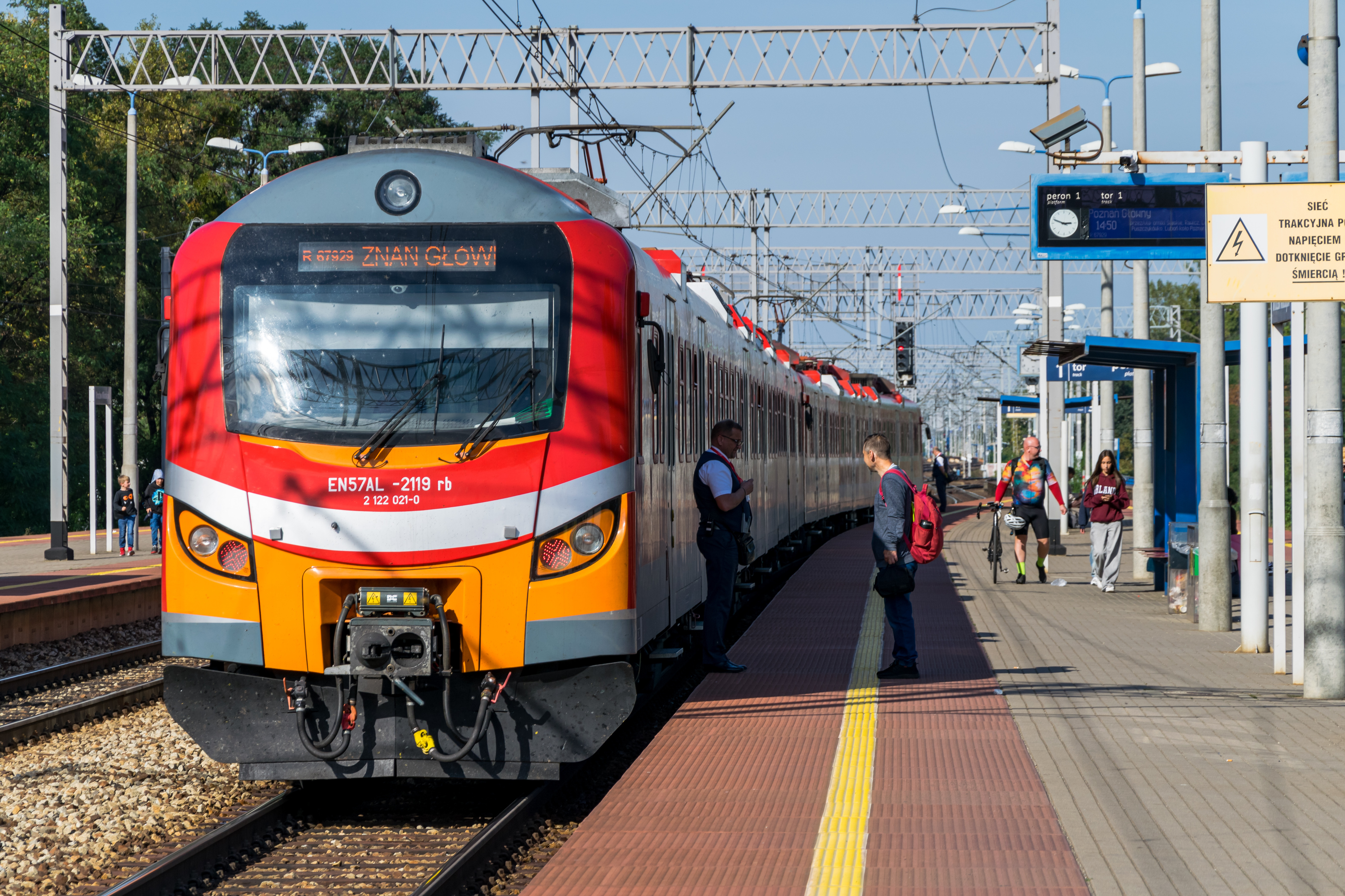 Double red-orange EN57AL stopped at a platform, there’s a train conductor talking to a traveller beside