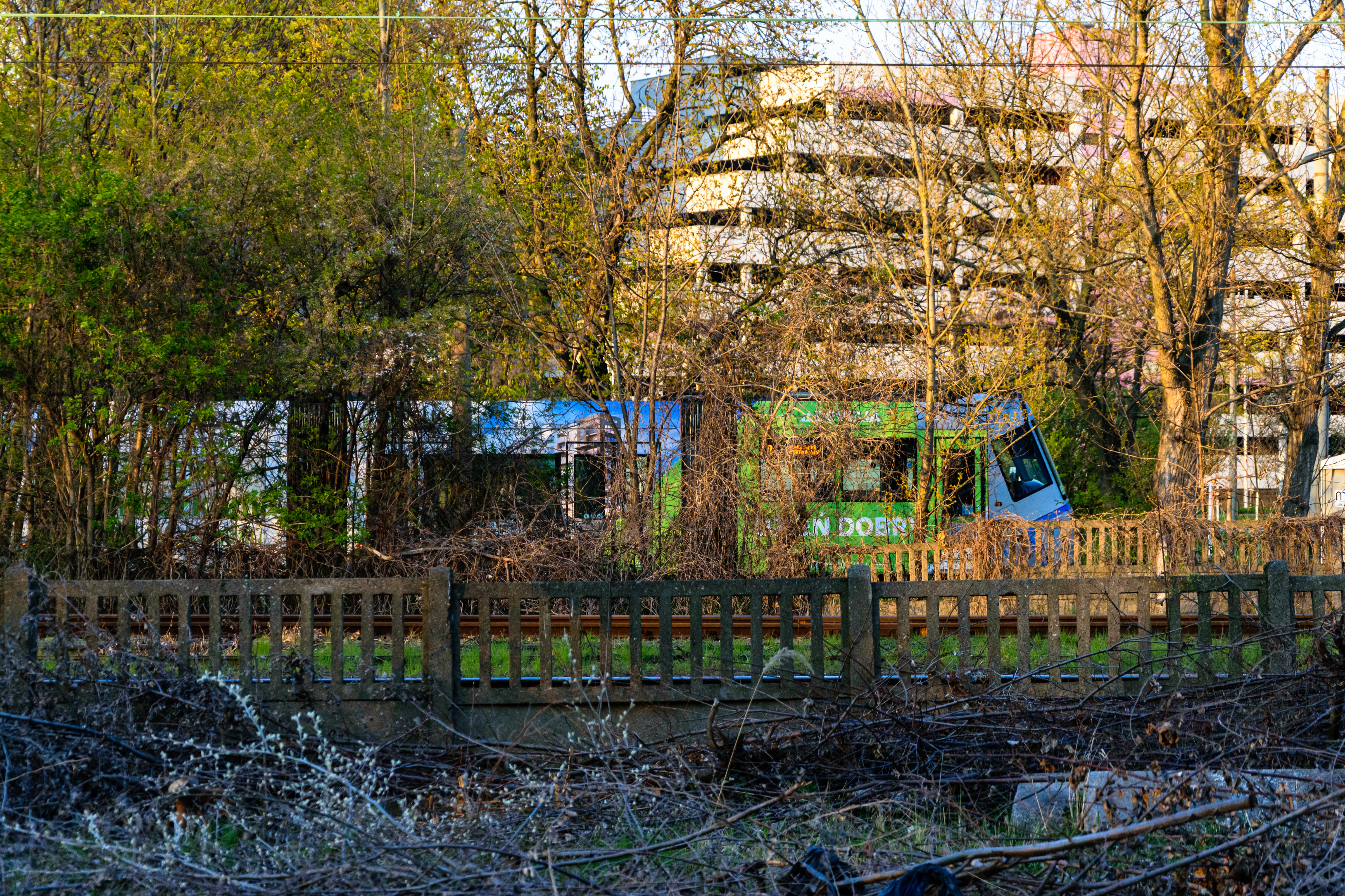 Silver-blue tram behind some trees and fences