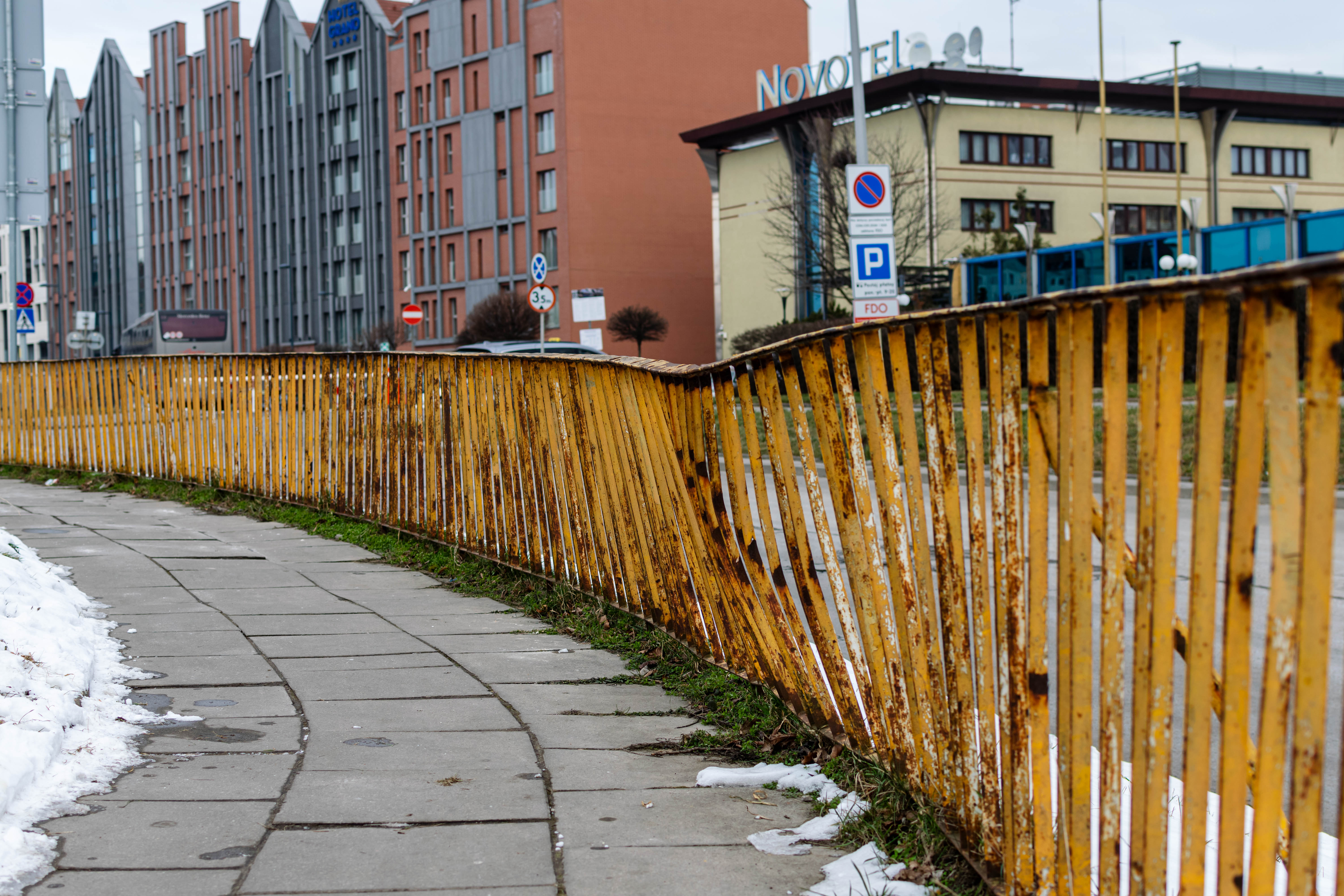 yellow rusted and damaged fence next to a grey sidewalk