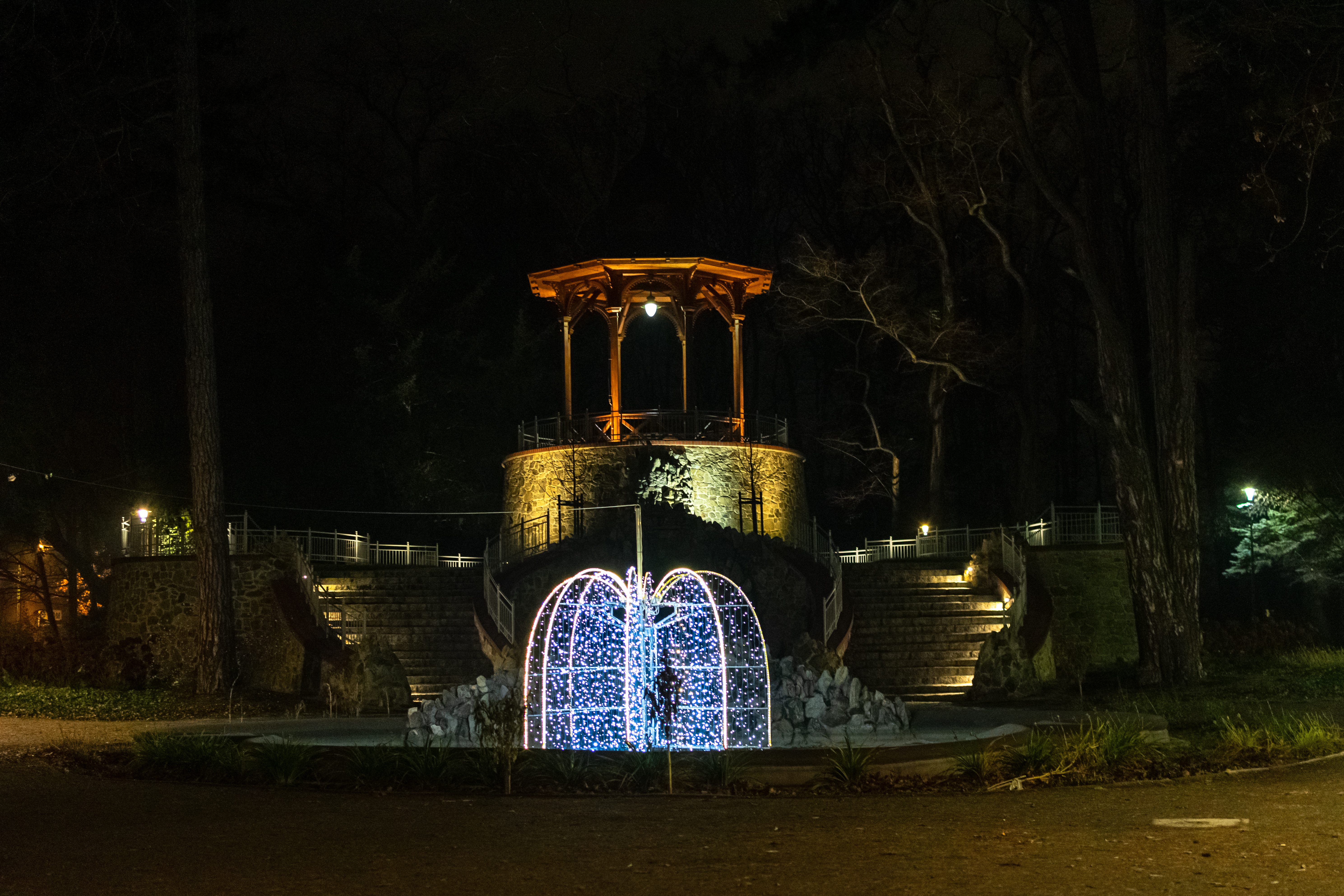 an illuminated gazebo with a fountain that has christmas decorations inside