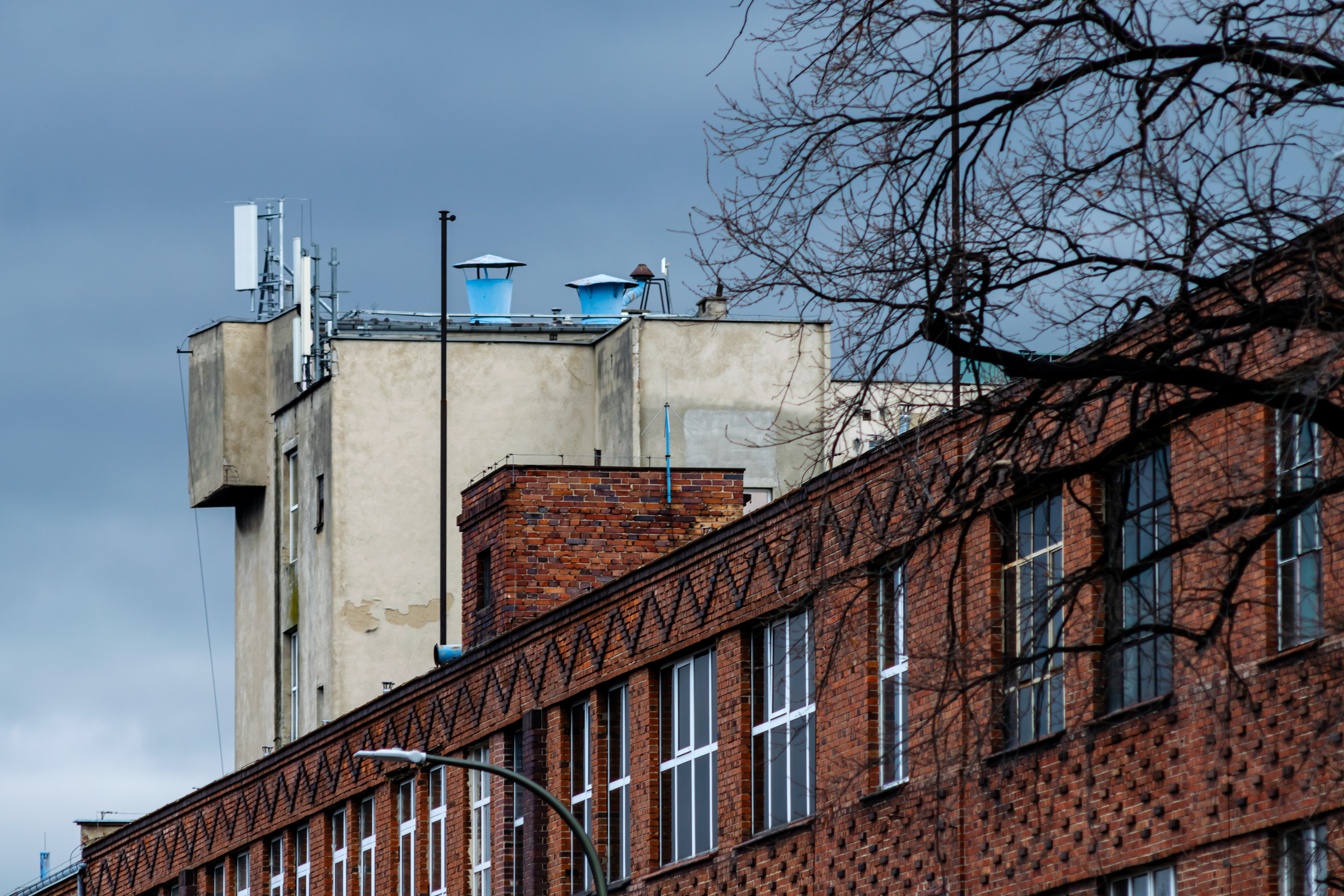 red brick factory building with some rather elaborate dark brick patterns around windows, there's a peaking building with a cell tower stuff on top