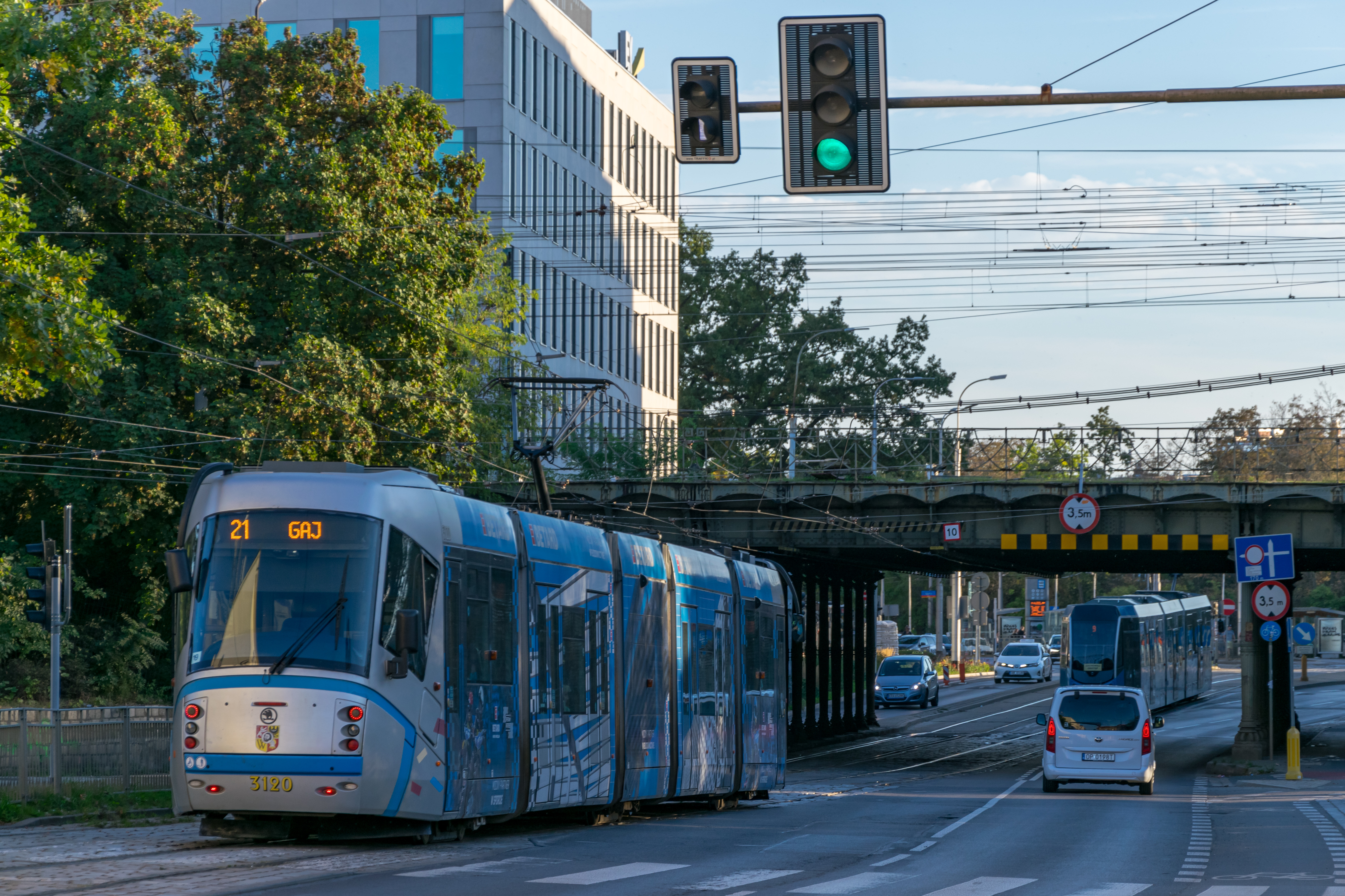 silver-blue tram wearing an ad livery soon to come under a train viaduct