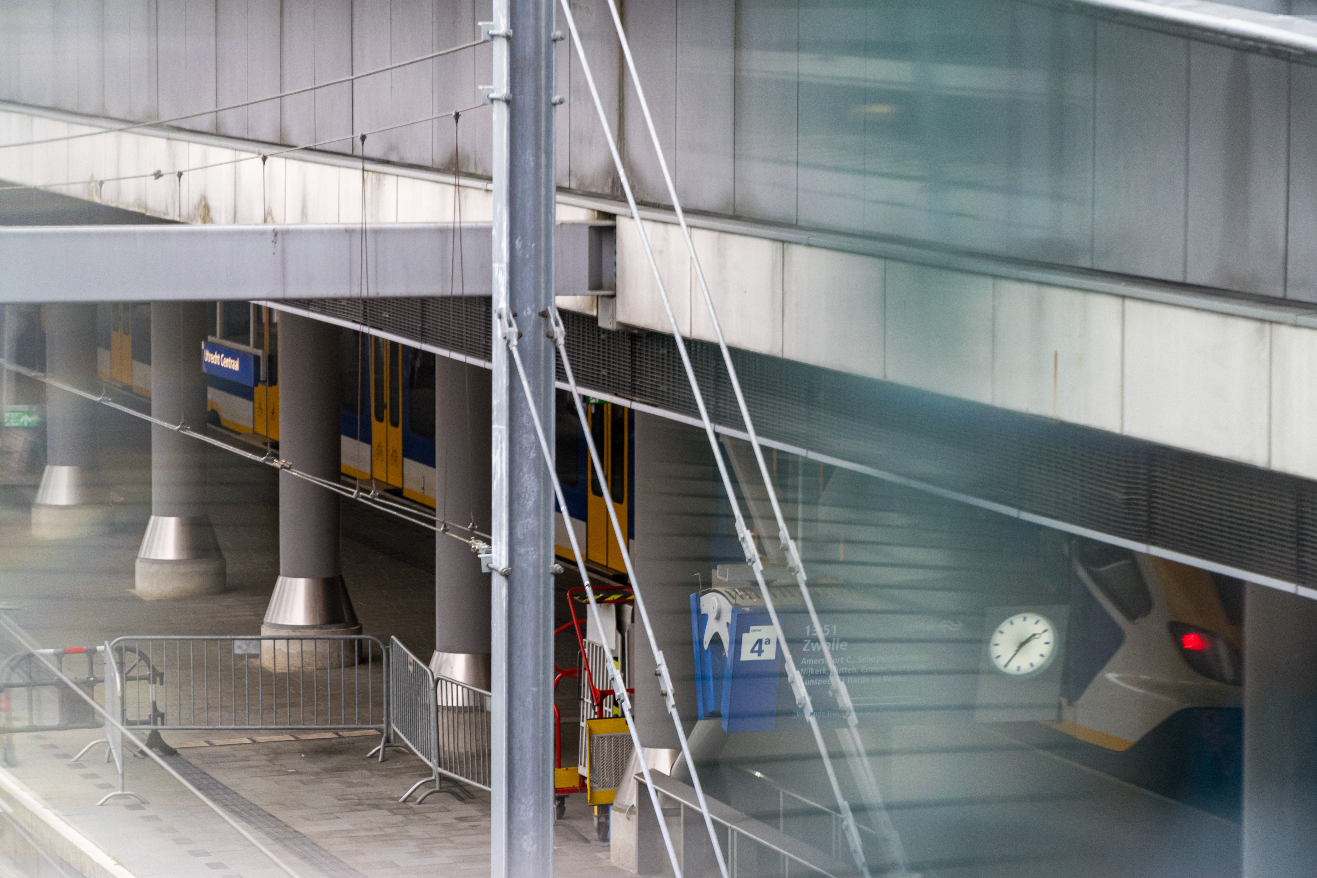 white-yellow-blue train at a platform, visible through some blurred glass panes