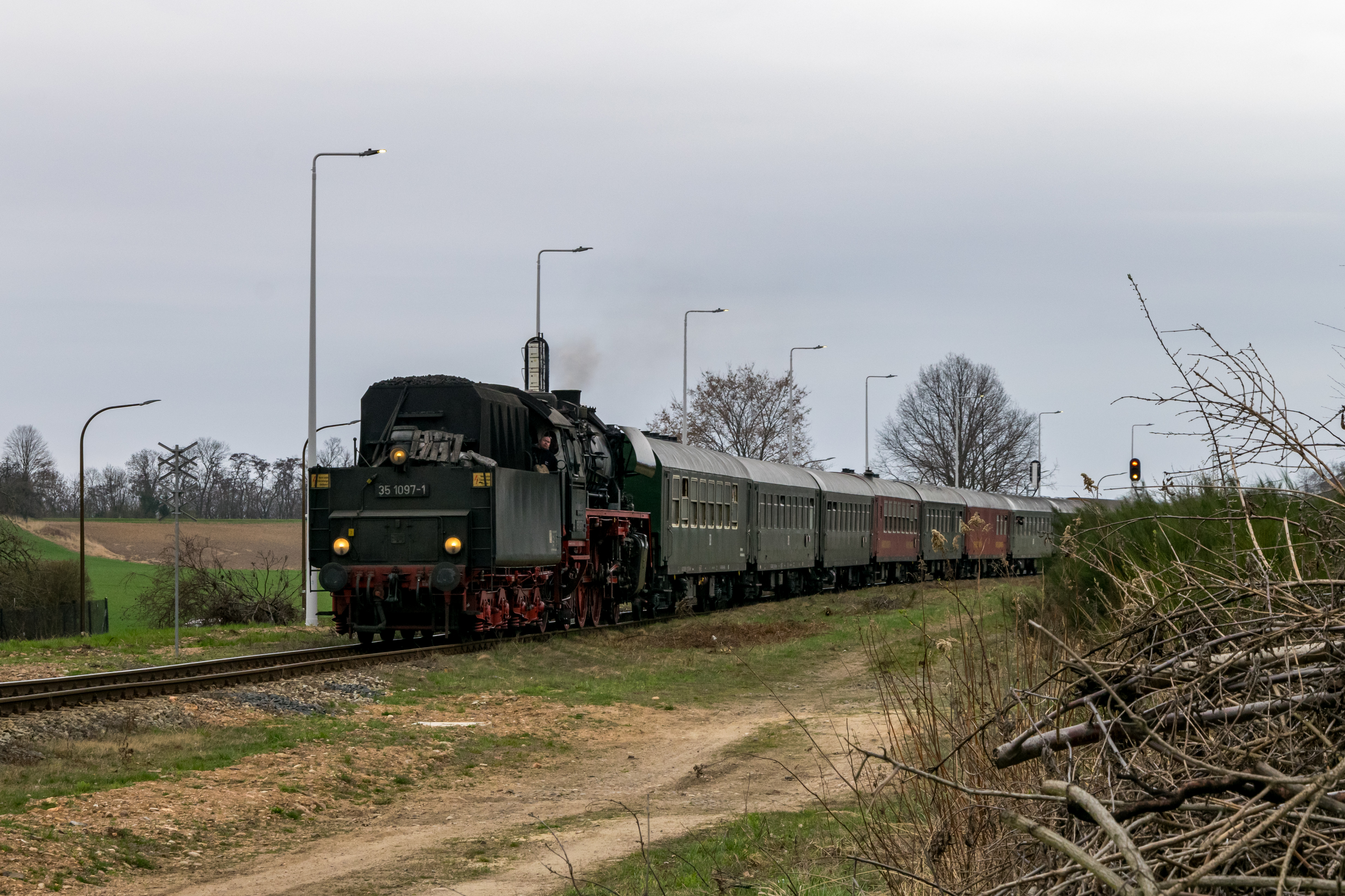 Train of 9 historic German coaches pulled by a steam locomotive in backwards, passing a junction