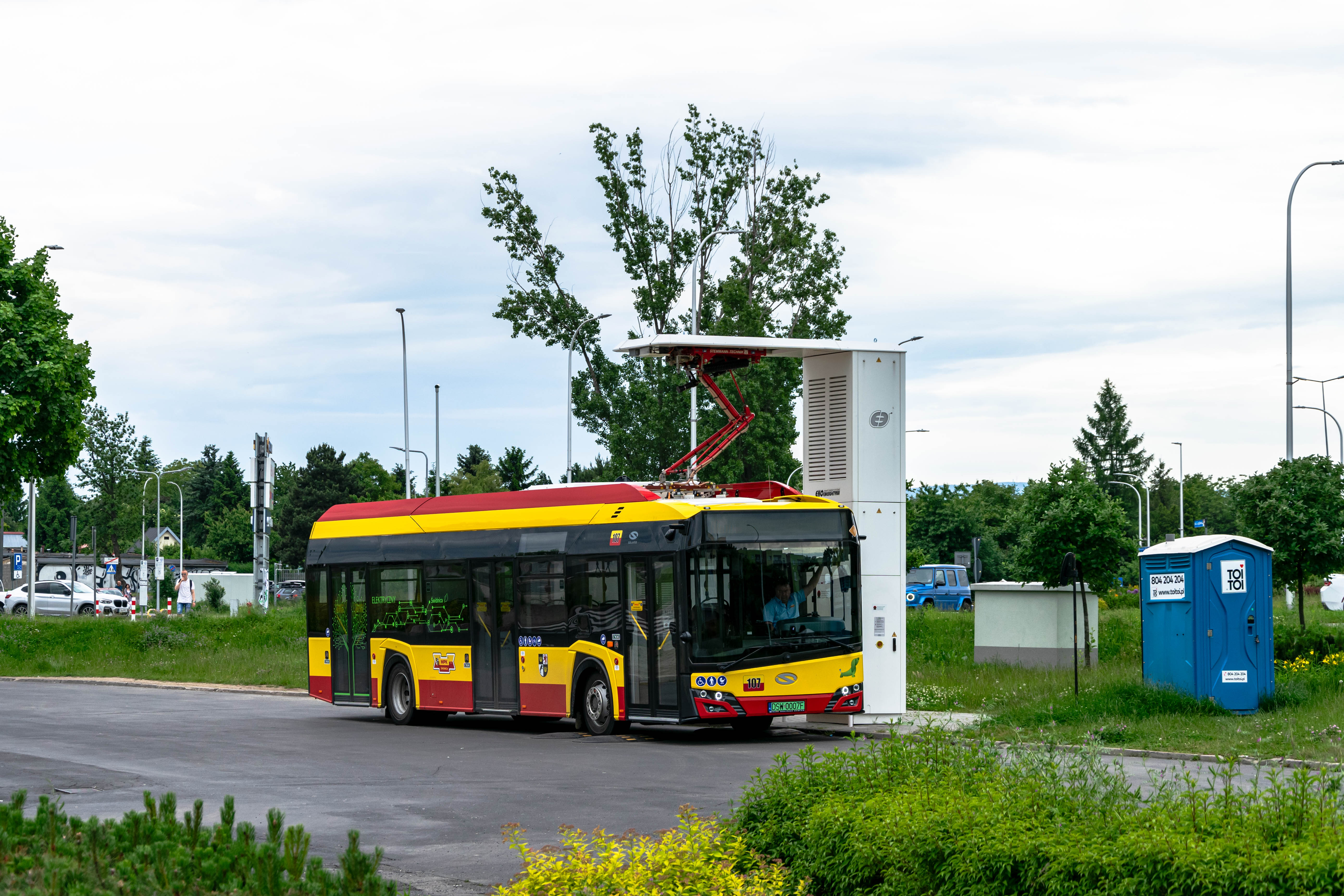 different yellow-red electric bus getting charged at a bus loop terminus