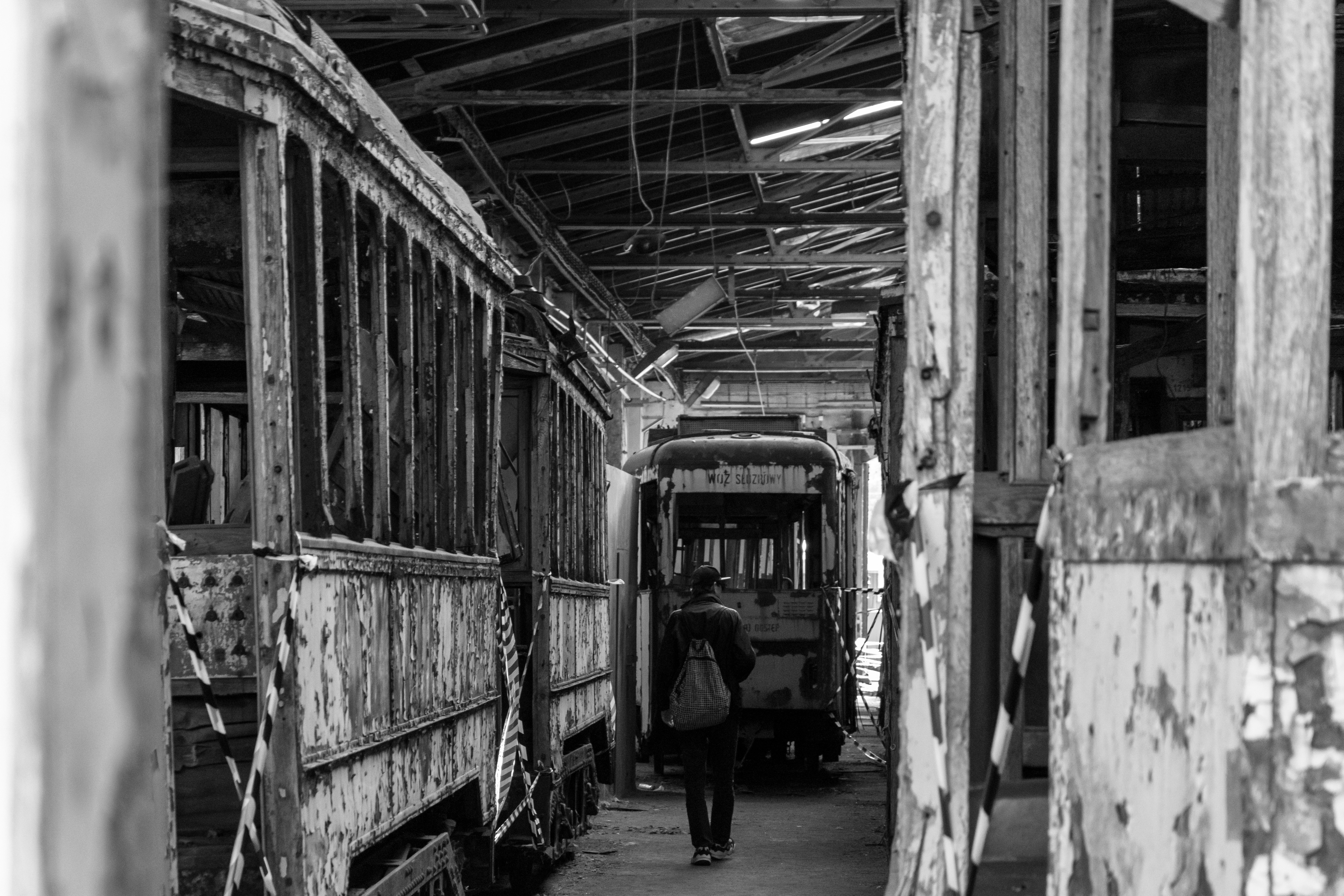 black and white photo showing a person walking between wrecks of wooden trams