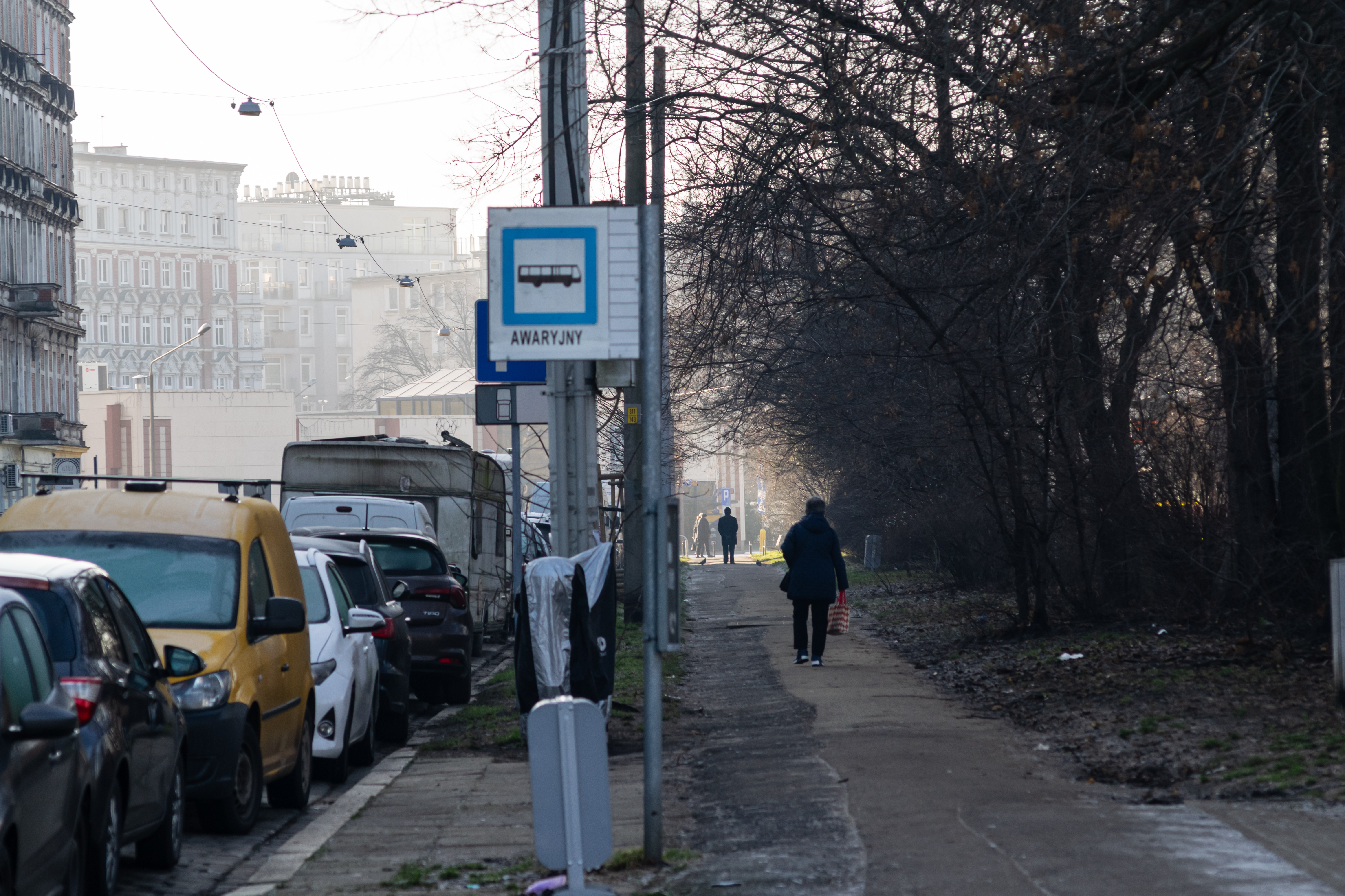 disused bus stop full of parked cars, there are people walking to the right of it