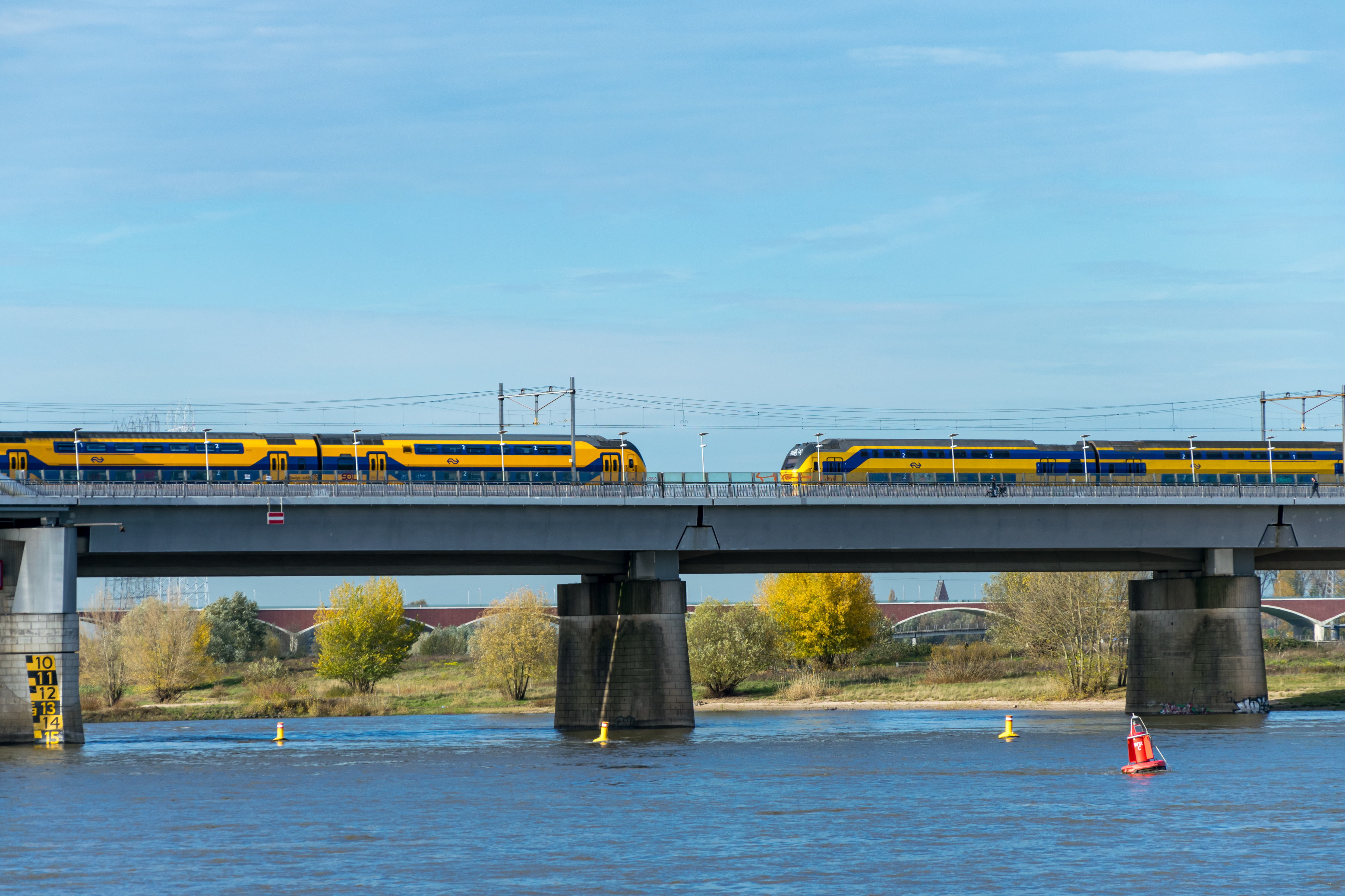 Two yellow-blue double decker trains on a bridge, viewed from side