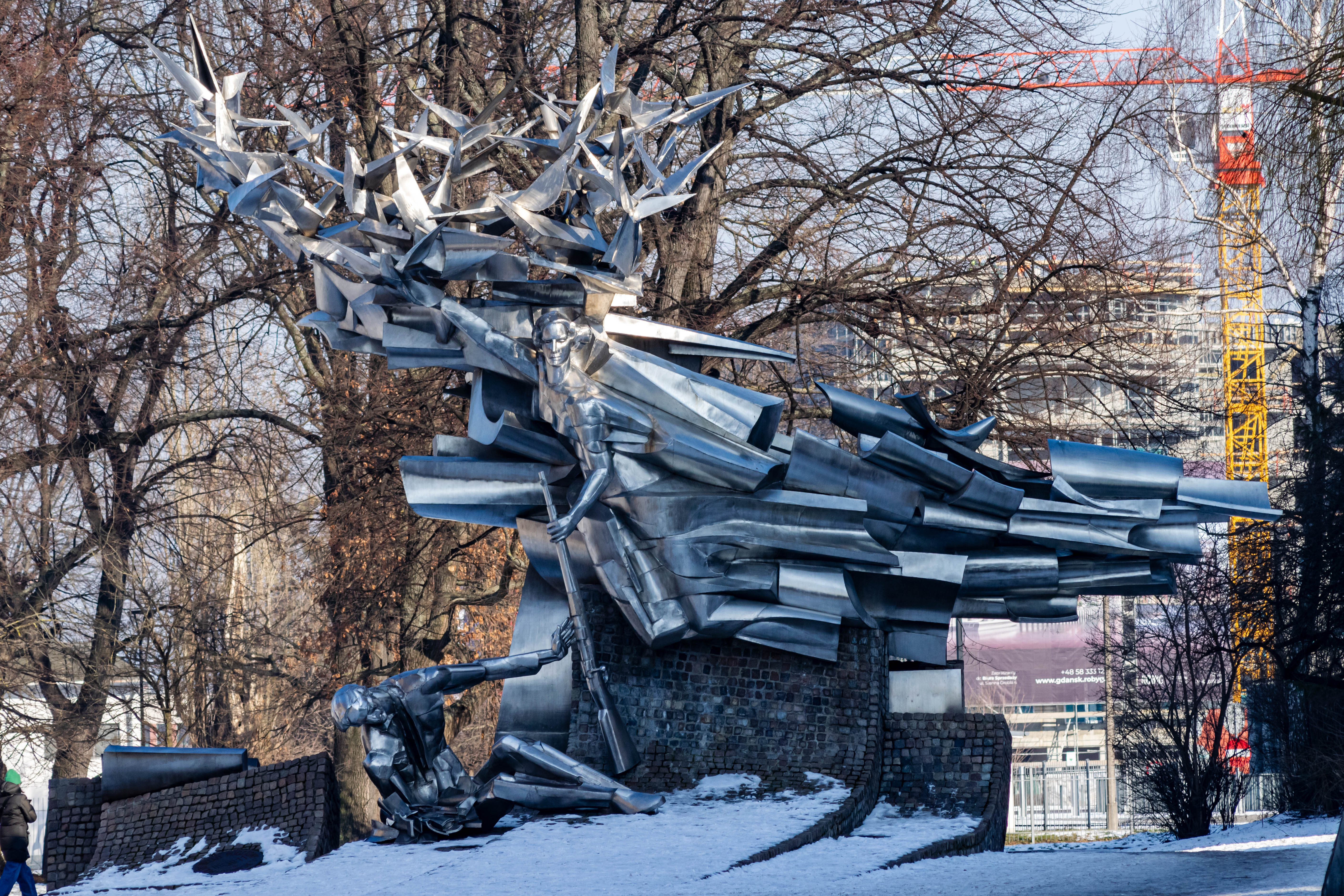 metal sculpture depicting struggle of two people defending a post office in gdańsk, with symbolic birds soaring above them