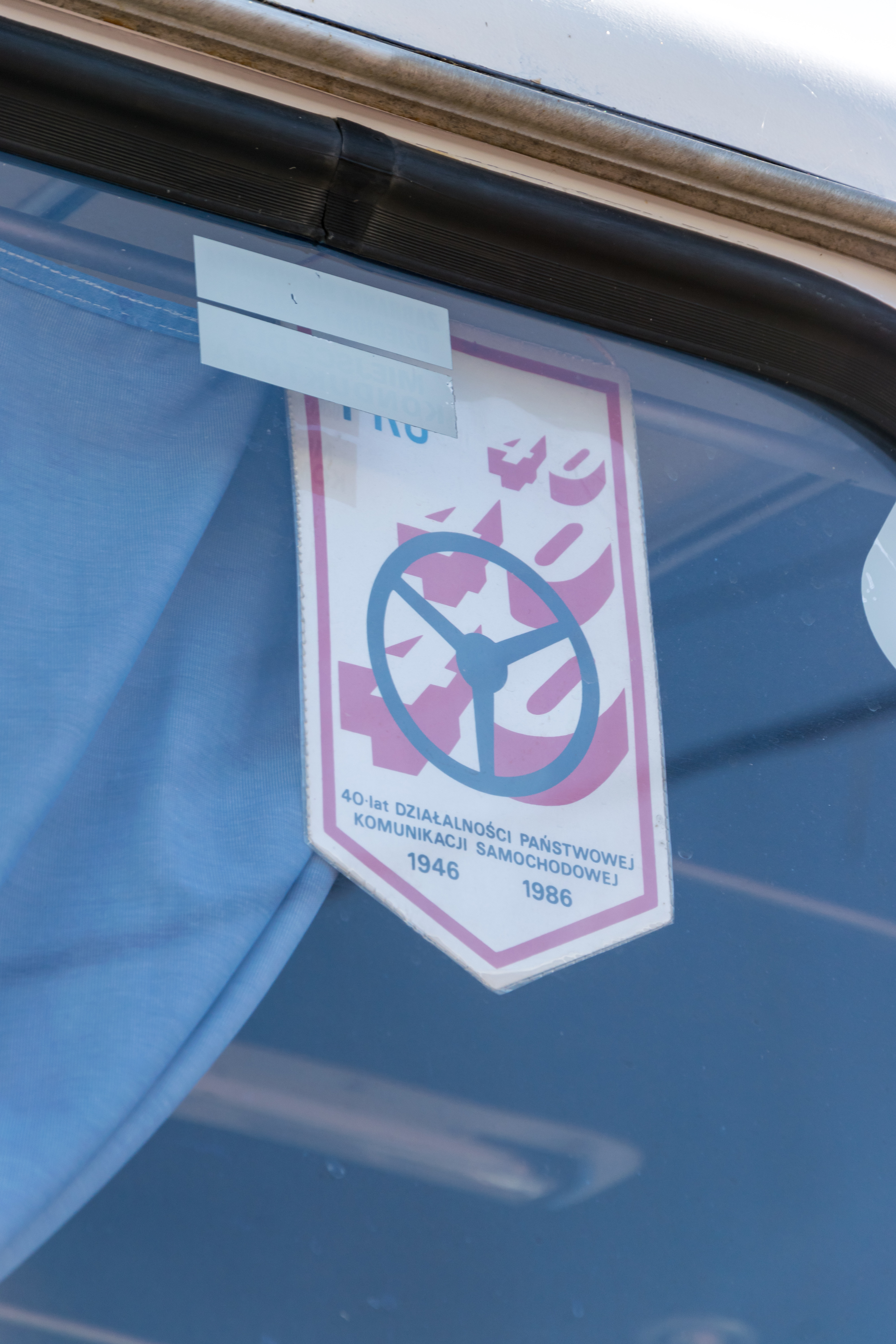 Small pennant celebrating 40 years of PKS activity from 1946 to 1986, featuring a steering wheel and three „40” symbols.