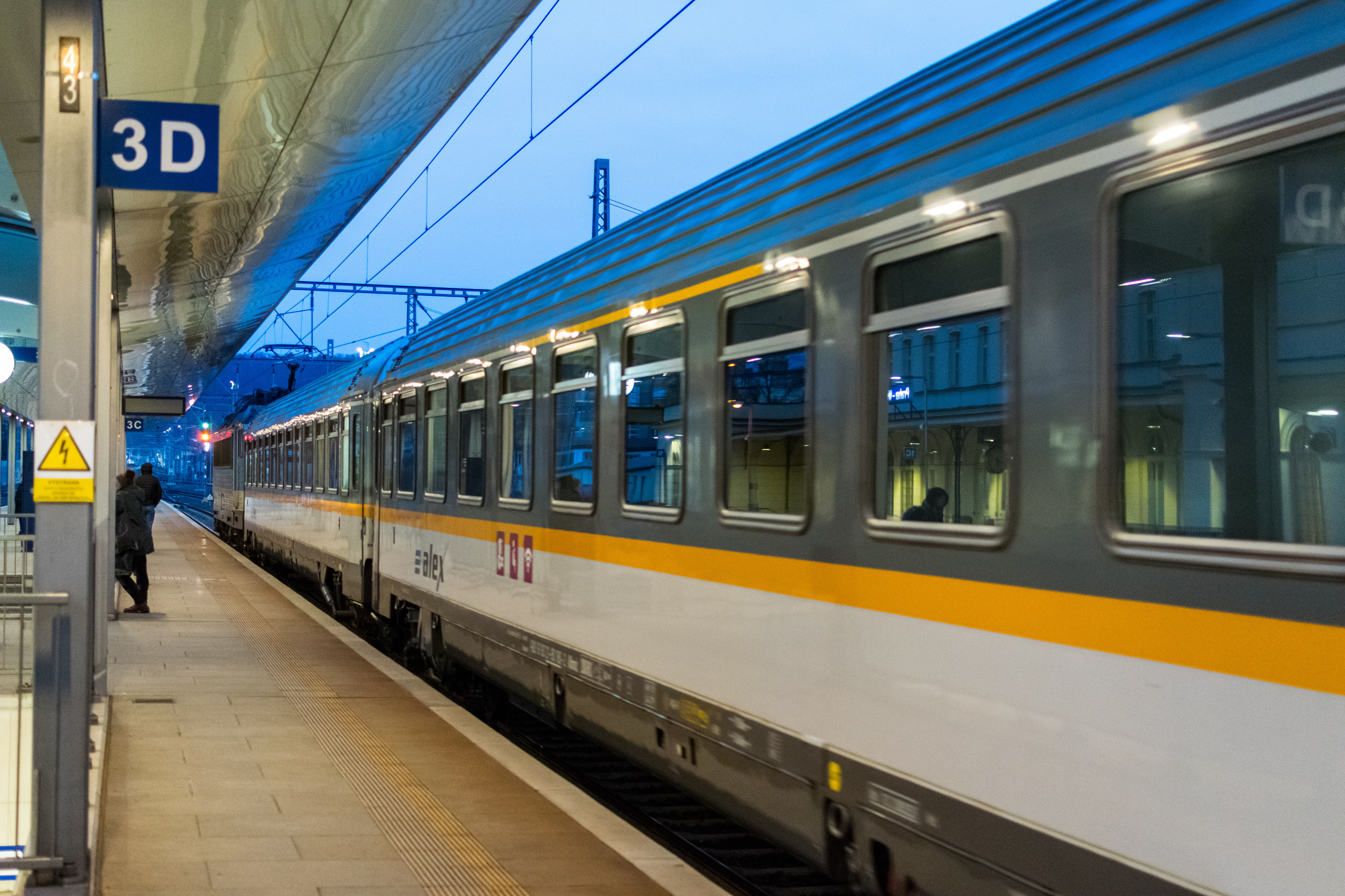 Train with blue locomotive and grey-yellow-white coaches speeding past the station