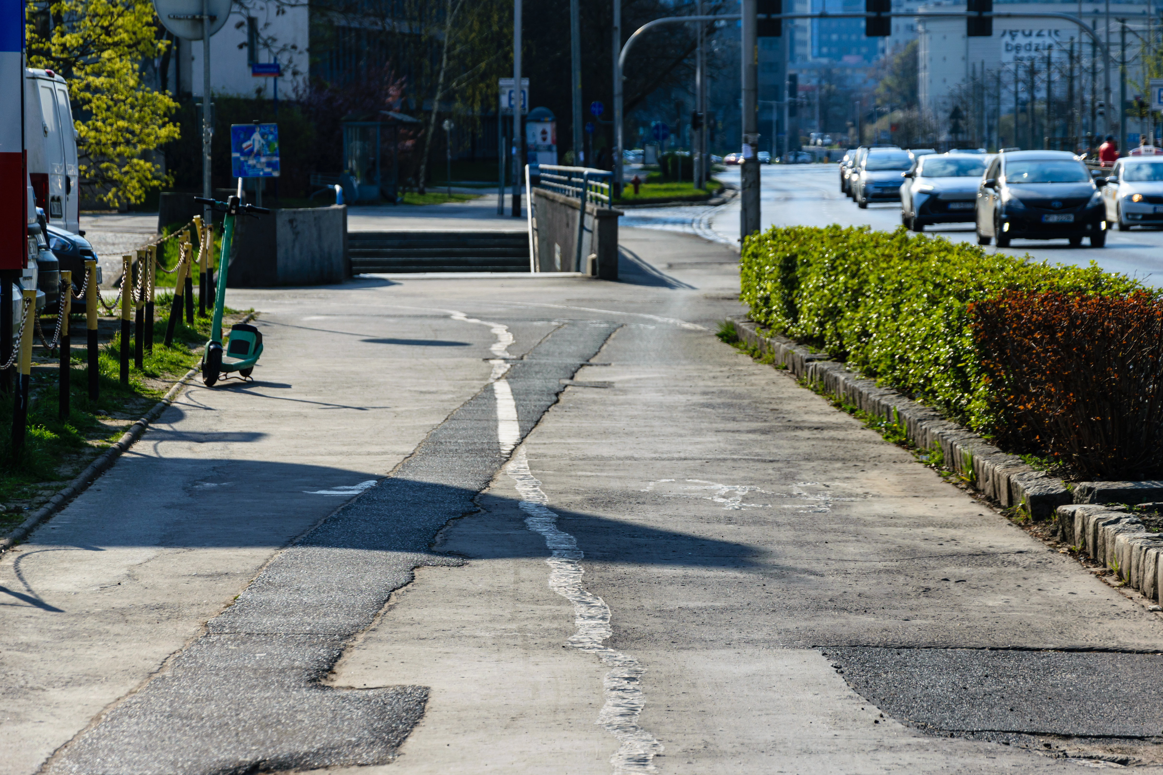 Asphalt sidewalk/bike path thing that is rather bad shape, there’s an e-scooter standing at the left