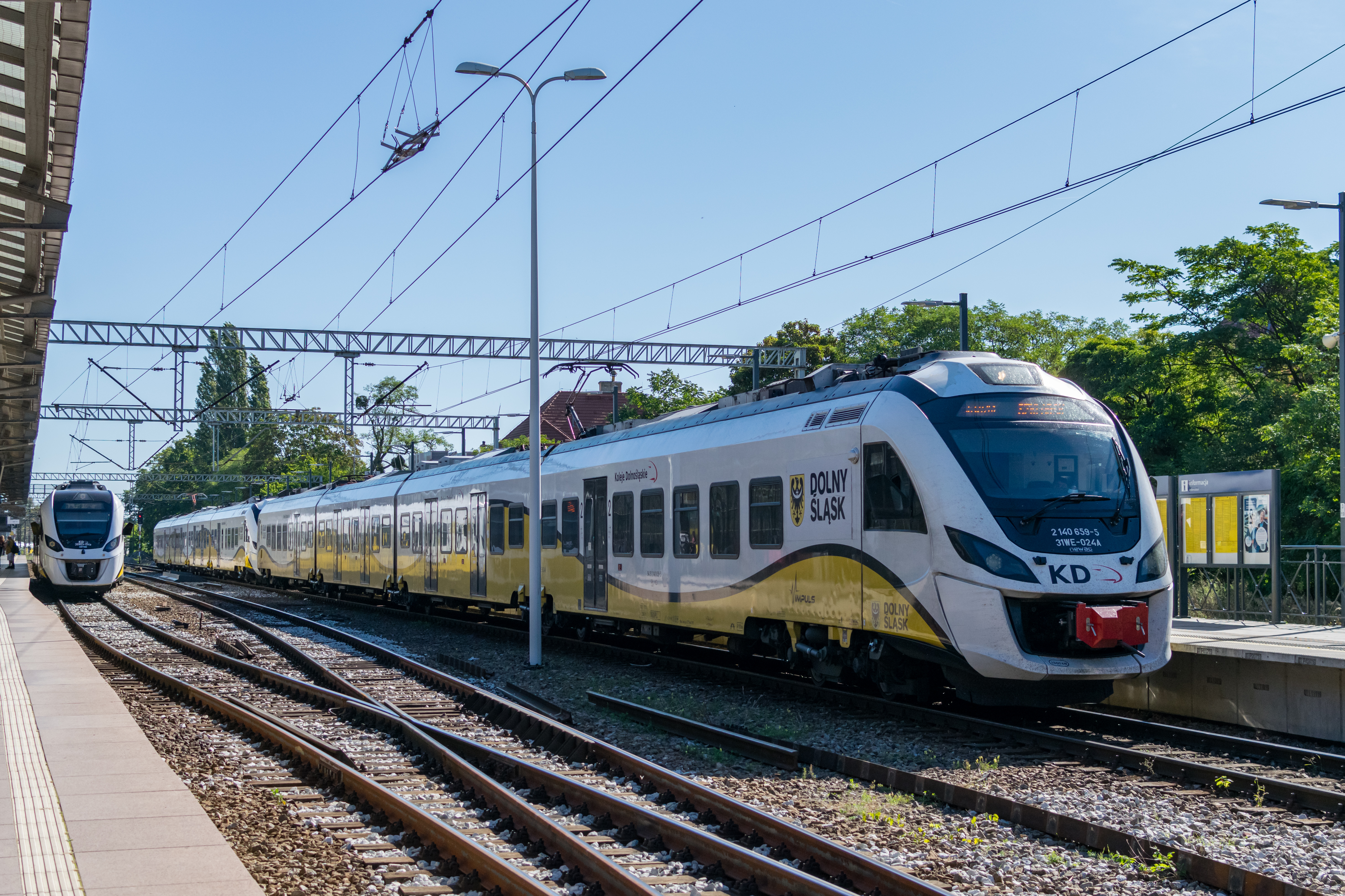 a train consisting of two coupled yellow-white 4-car units, with another yellow-white train in background