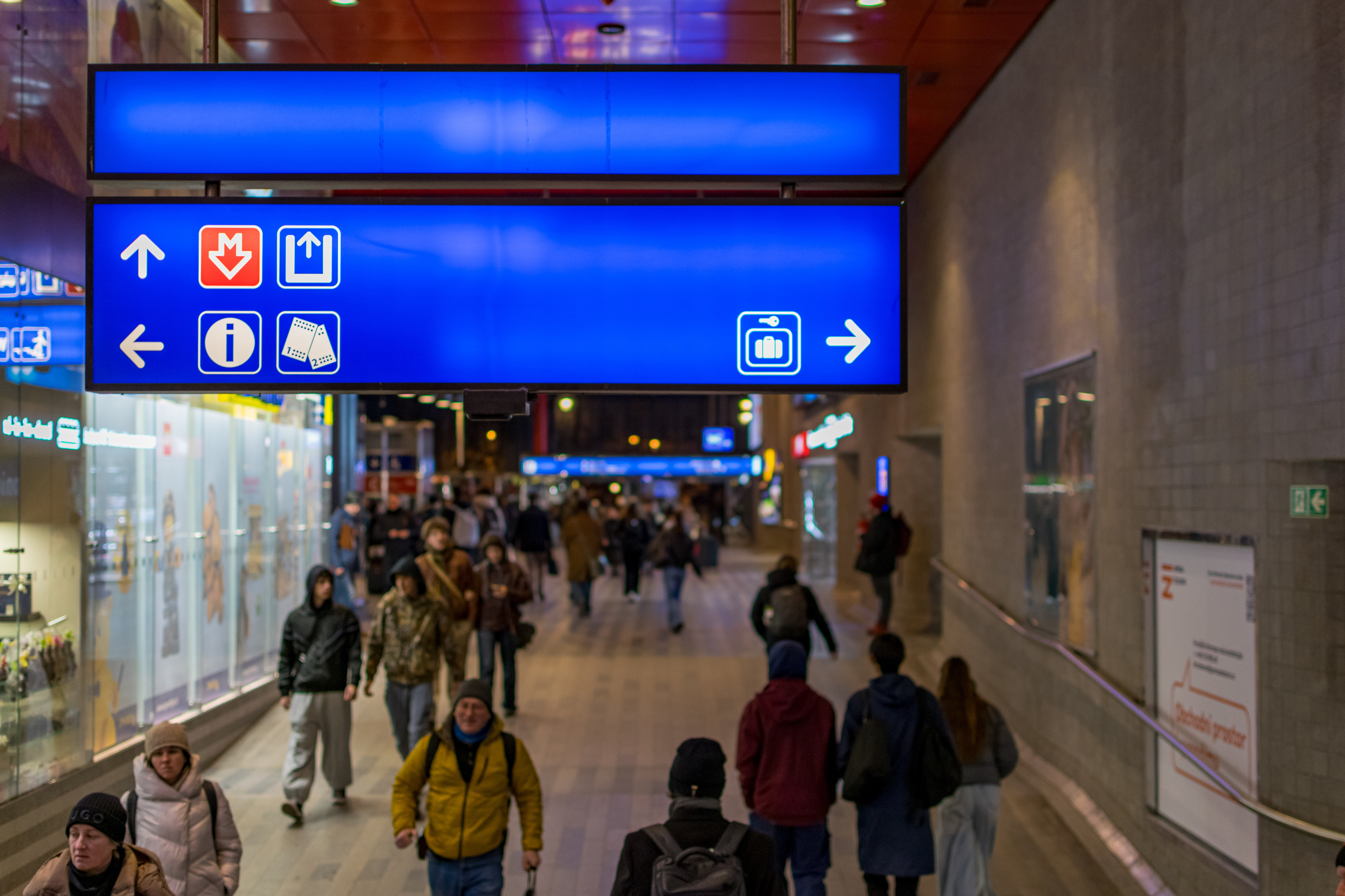 Interior of a train station, with focus on an illuminated sign, most people are out of focus