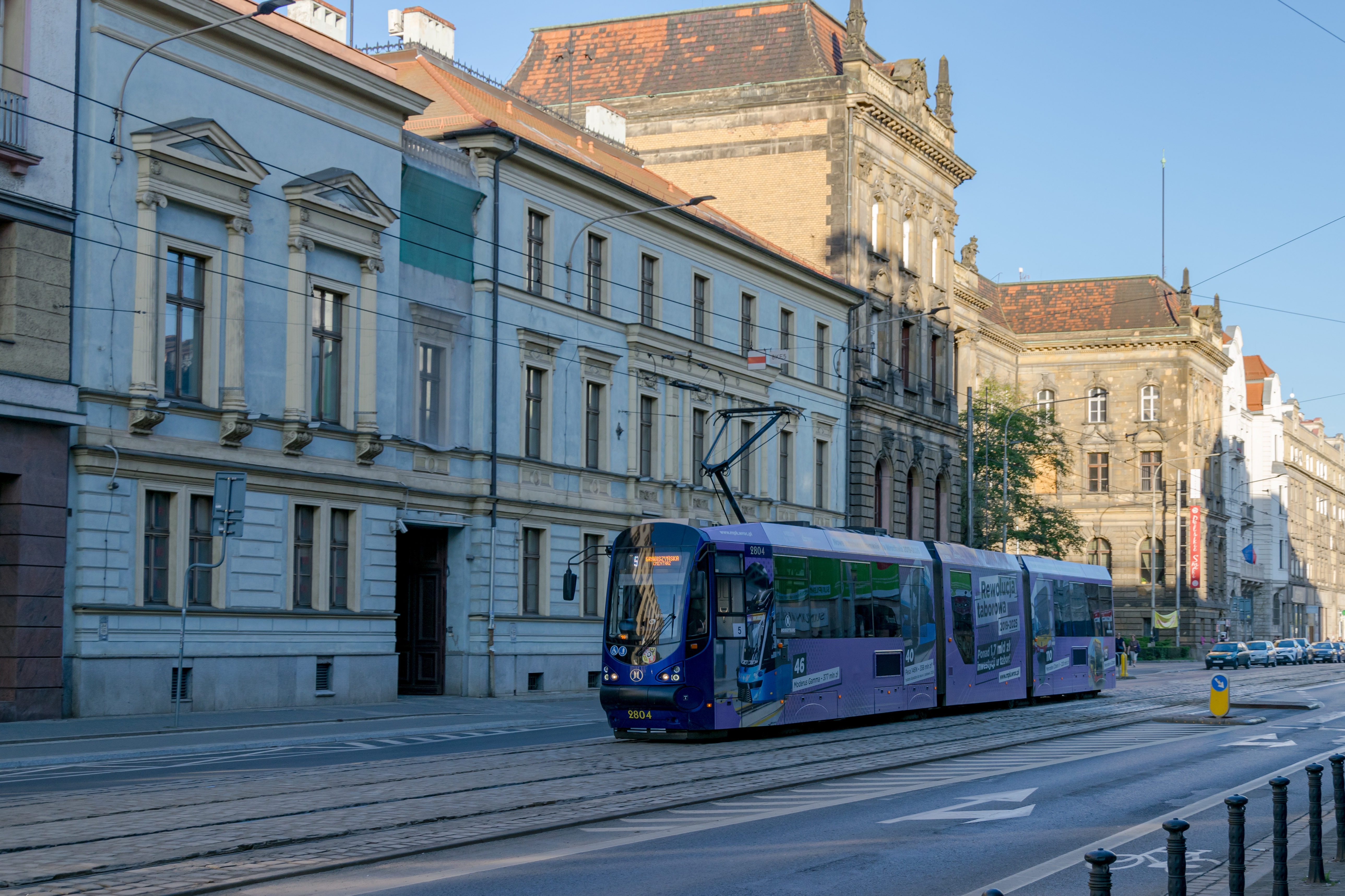 dark-blue tram wearing an ad livery with old buildings in background