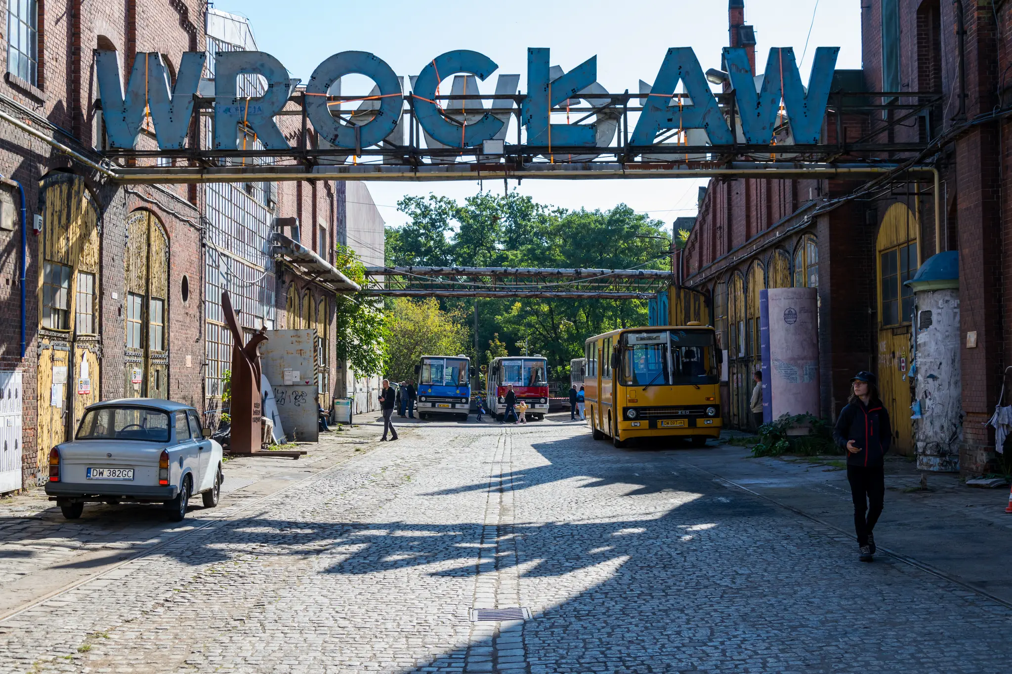 Old Wrocław Główny sign put few meters above street, with a bunch of Ikarus buses visible in background