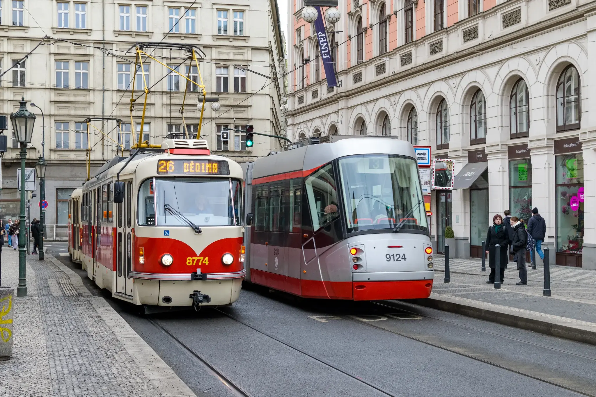 old white-red tram next to a more modern silver-red tram at a tram stop