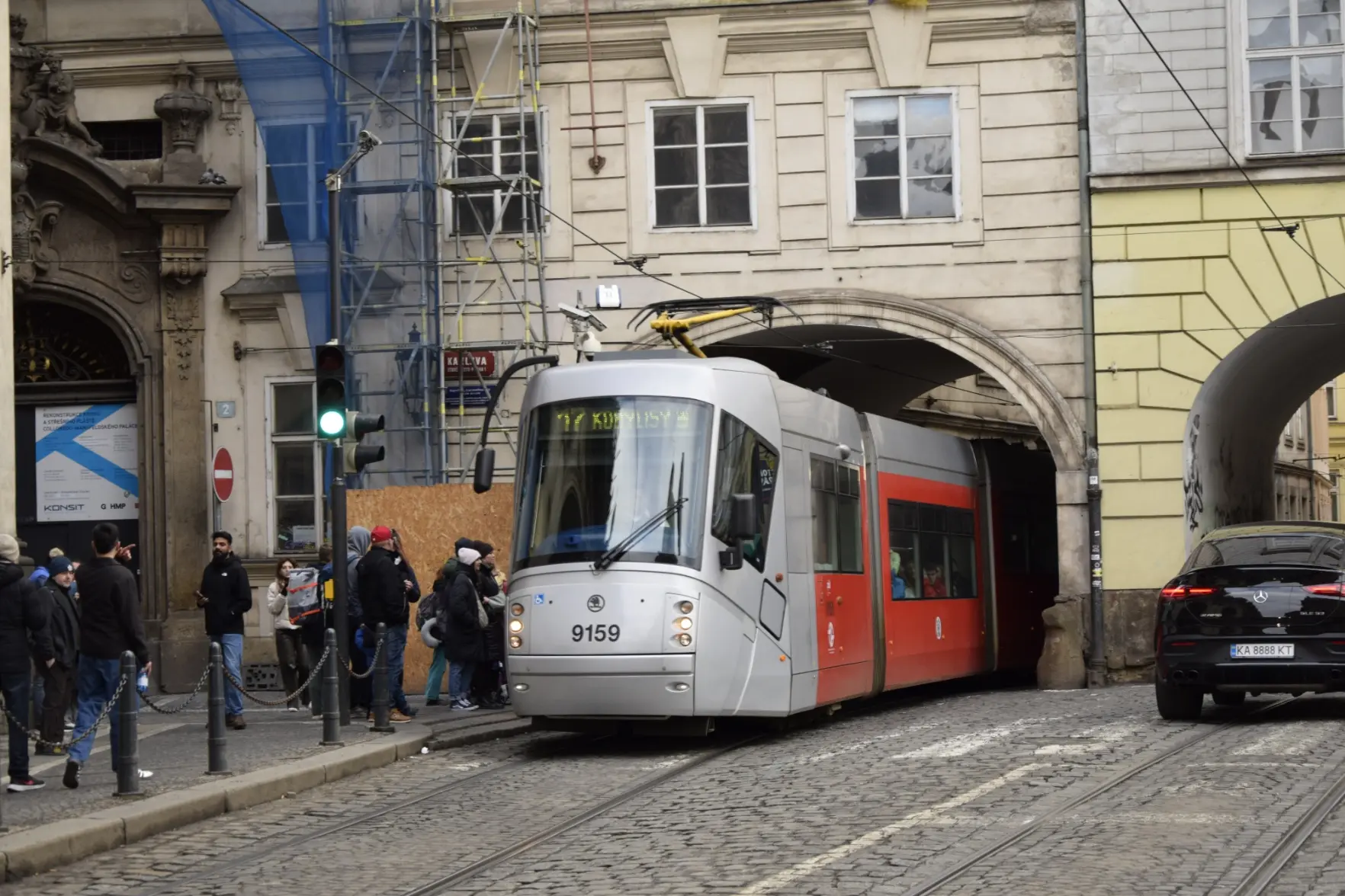 Grey-red tram leaving a very tight arch of a building, with pantograph being very lowered because the arch barely fits the tram anyway