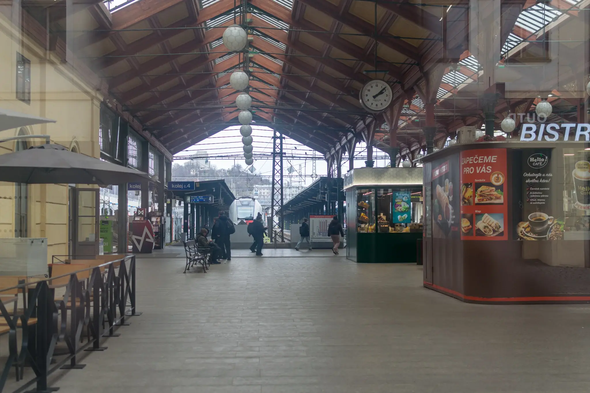 train shed with a bunch of kiosks and benches, with a train in background