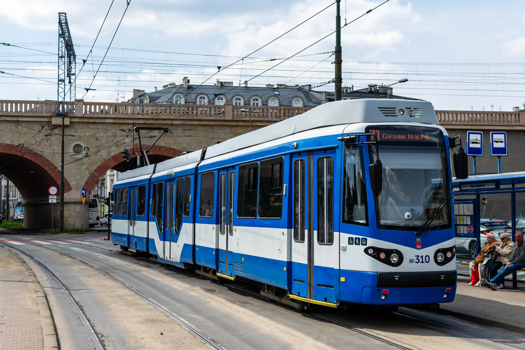 Blue-white tram at a stop, next to a railway bridge