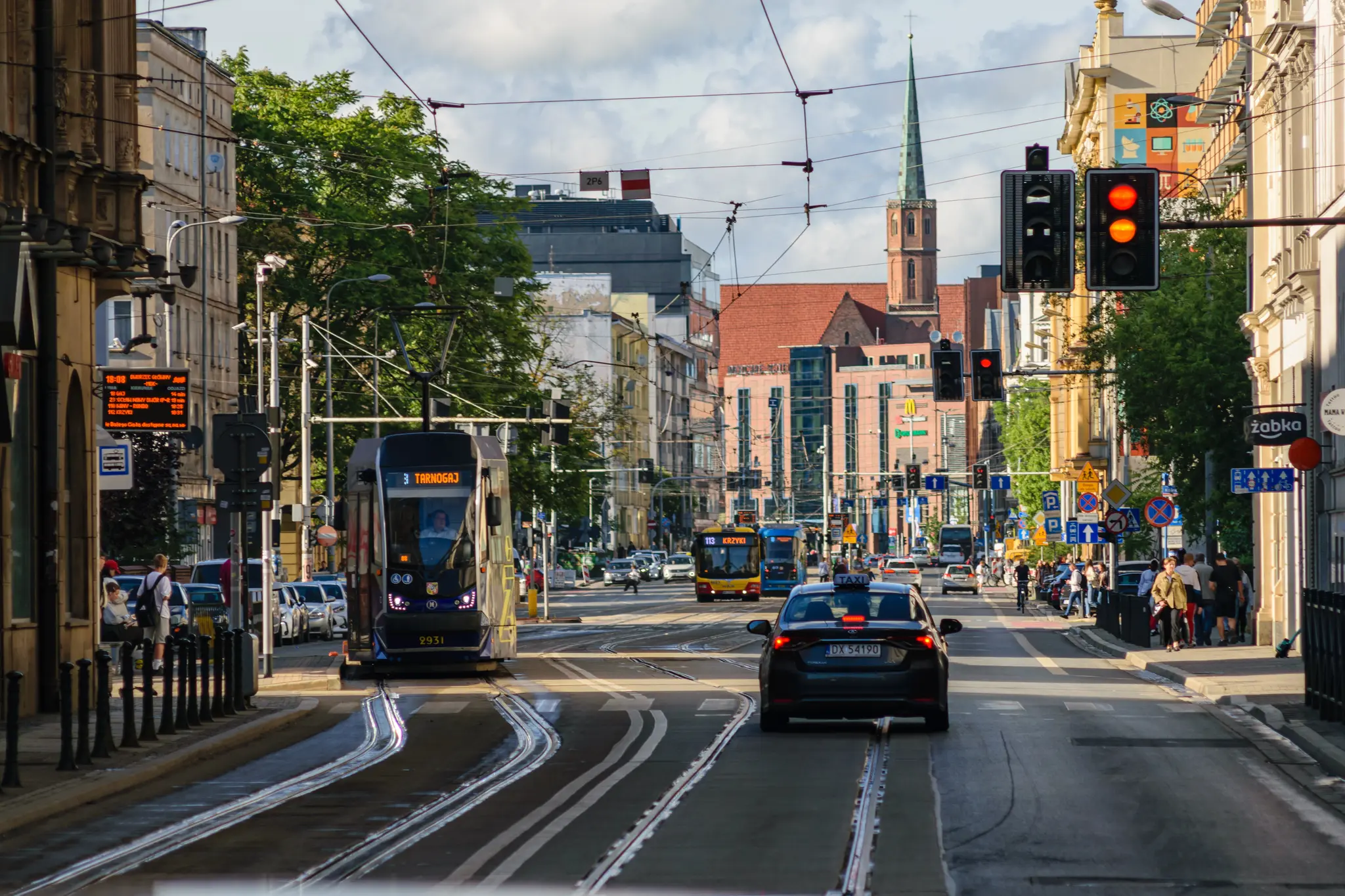 Blue tram at a stop, around old city architecture, there’s another tram and a bus in background