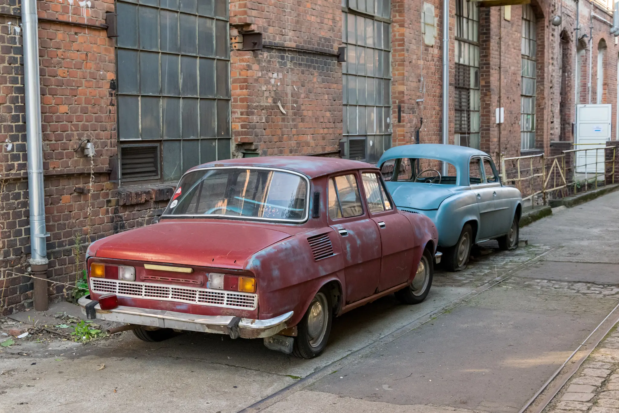 not working red Škoda 100, alongside a blue unidentified car without windows