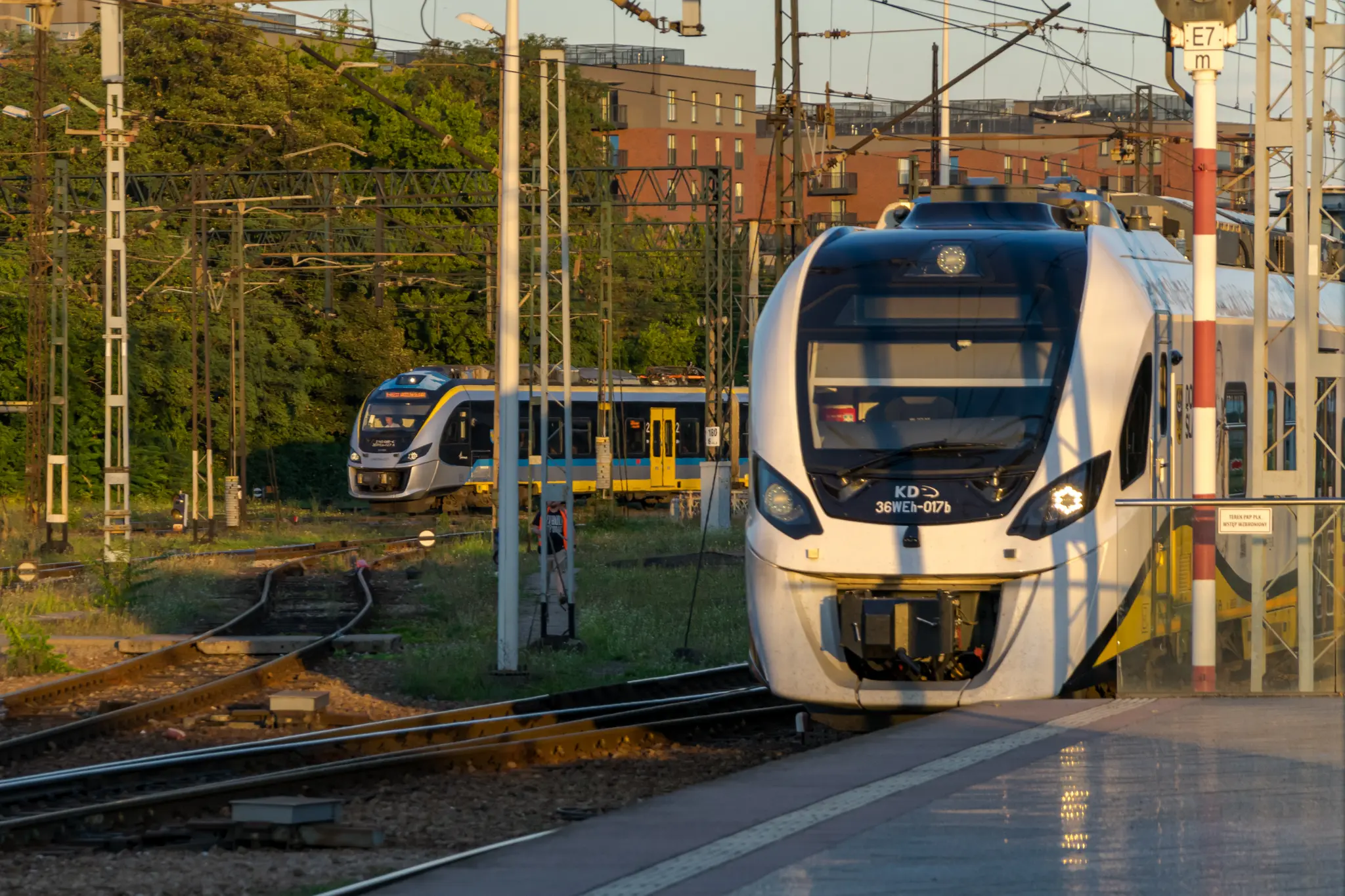 two trains, closer to camera is a yellow-white impuls 2 arriving at a platform, in background a silver-blue-yellow-black impuls 1