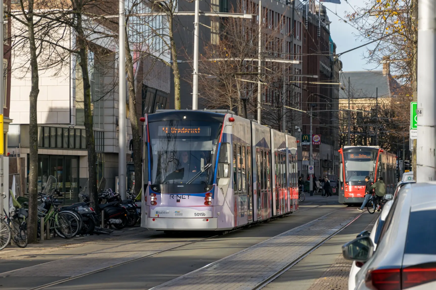modern blue-ish tram on a street, there's another red tram in background