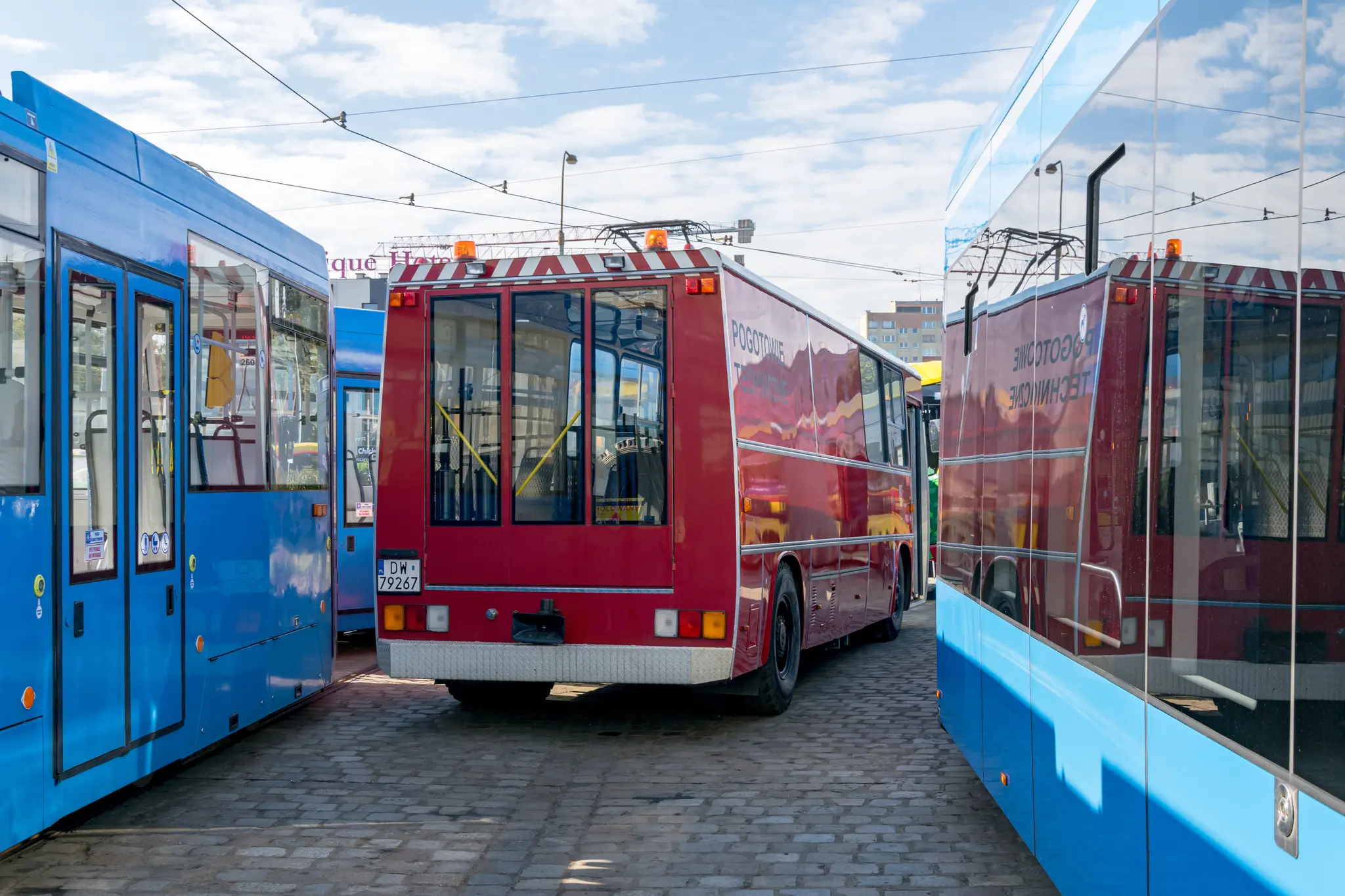 Back of red Ikarus 260 bus converted into a technical vehicle, showing three-leafed doors, bus is sandwiched between two trams