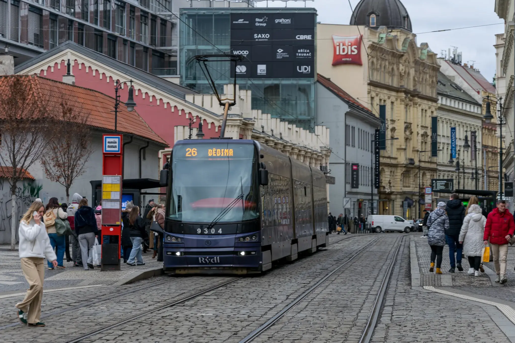 blue-ish tram in ad livery leaving a tram stop