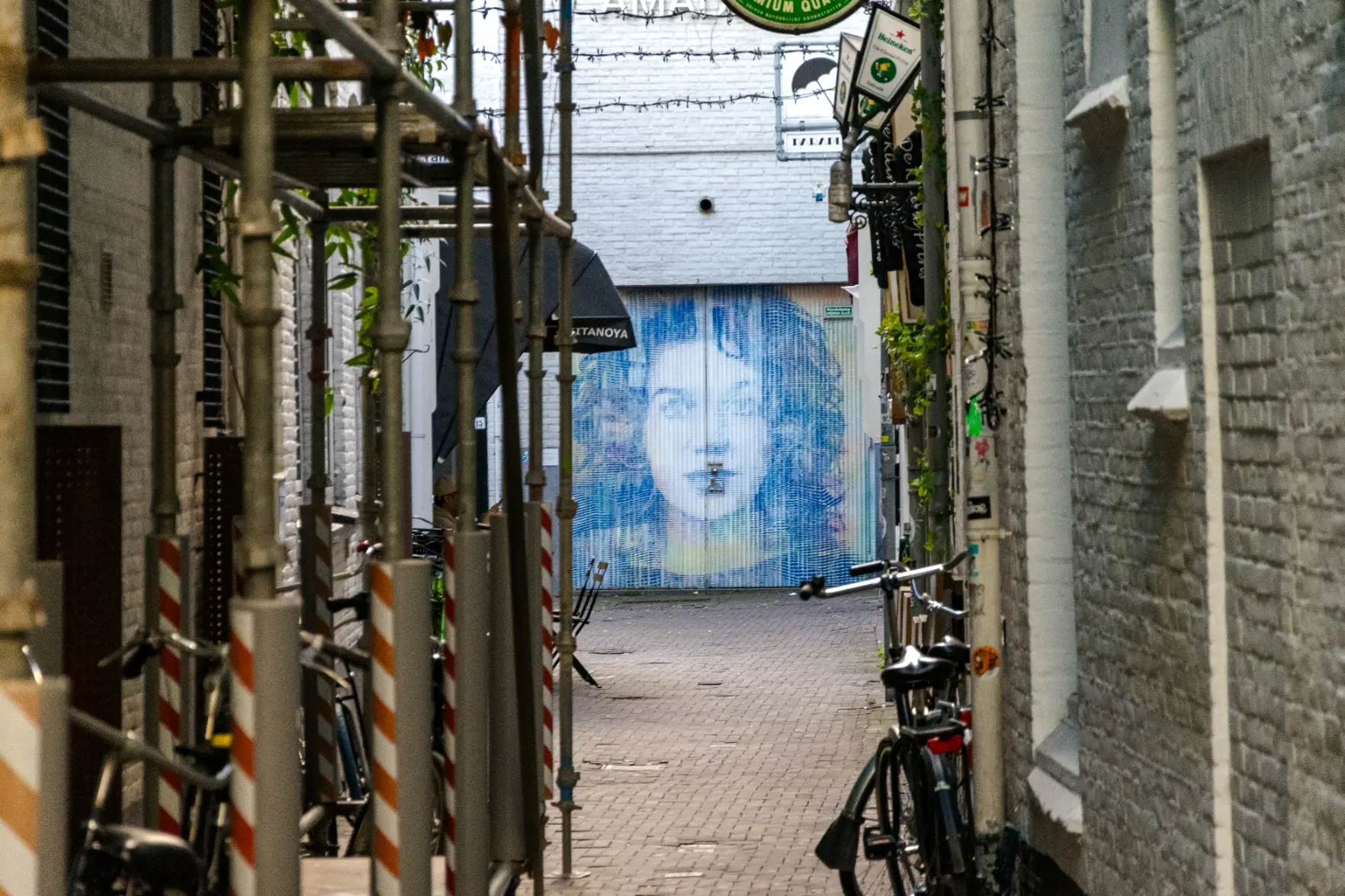 narrow street with a graffiti/mural of a woman on doors at the end